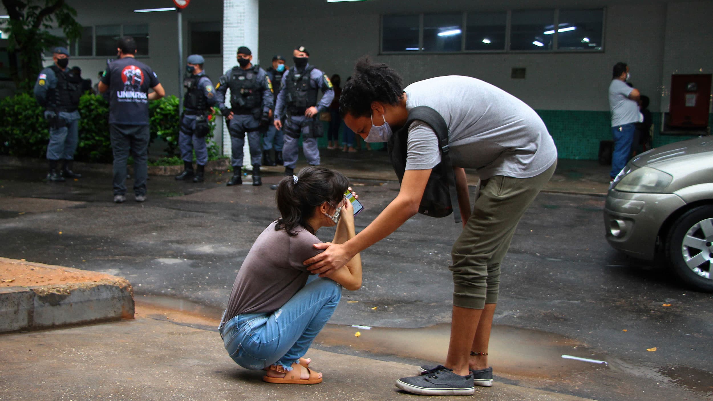 A woman is show with her face in her hands and crouched down with a man next to her with his hand on her shoulder.