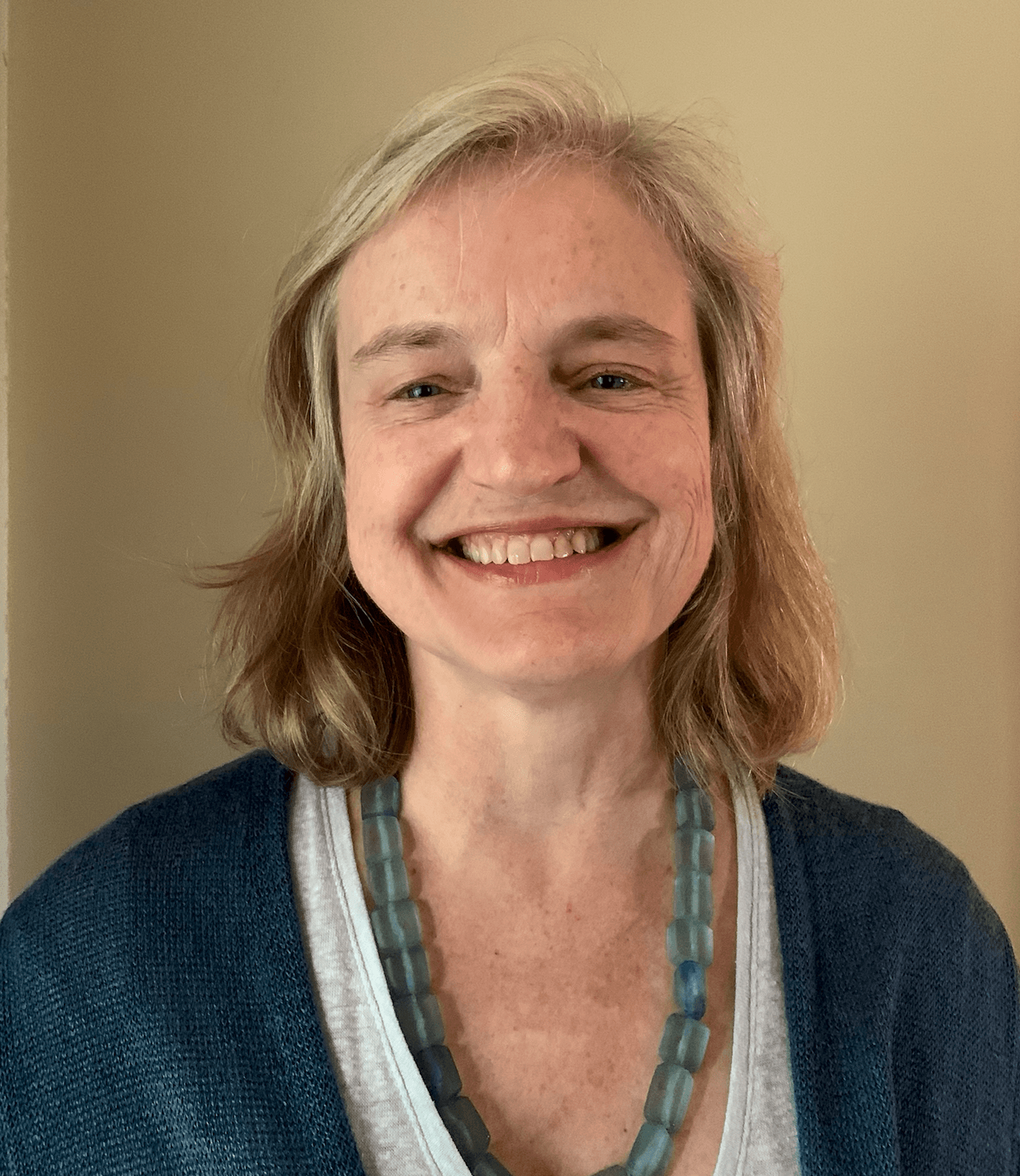 a woman wearing a blue sweater and necklace smiles.