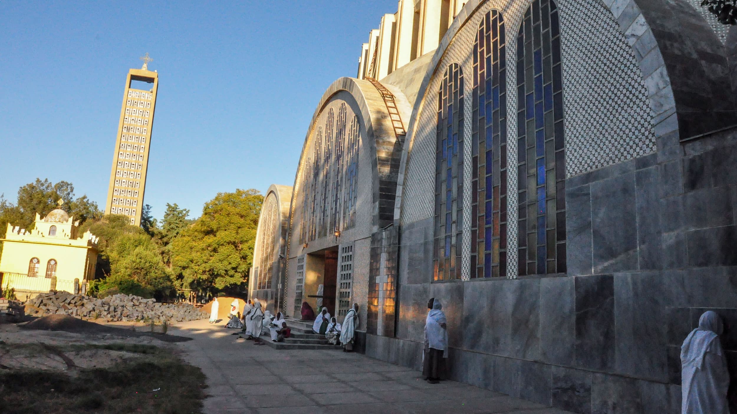 The Church of St. Mary of Zion in Axum is shown with its three rounded arcs with stain-glass windows and several people out from.
