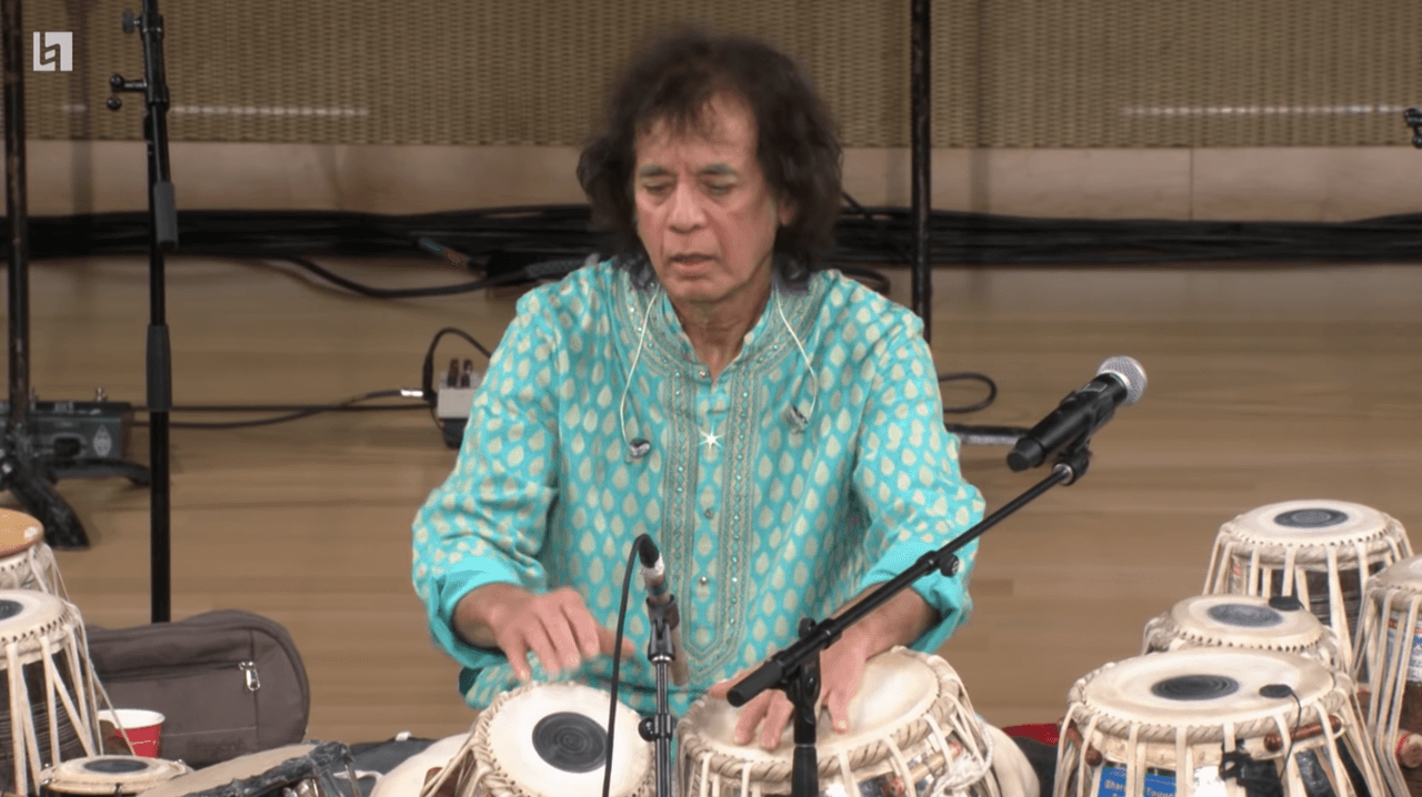 A man plays tabla while wearing a light blue shirt.