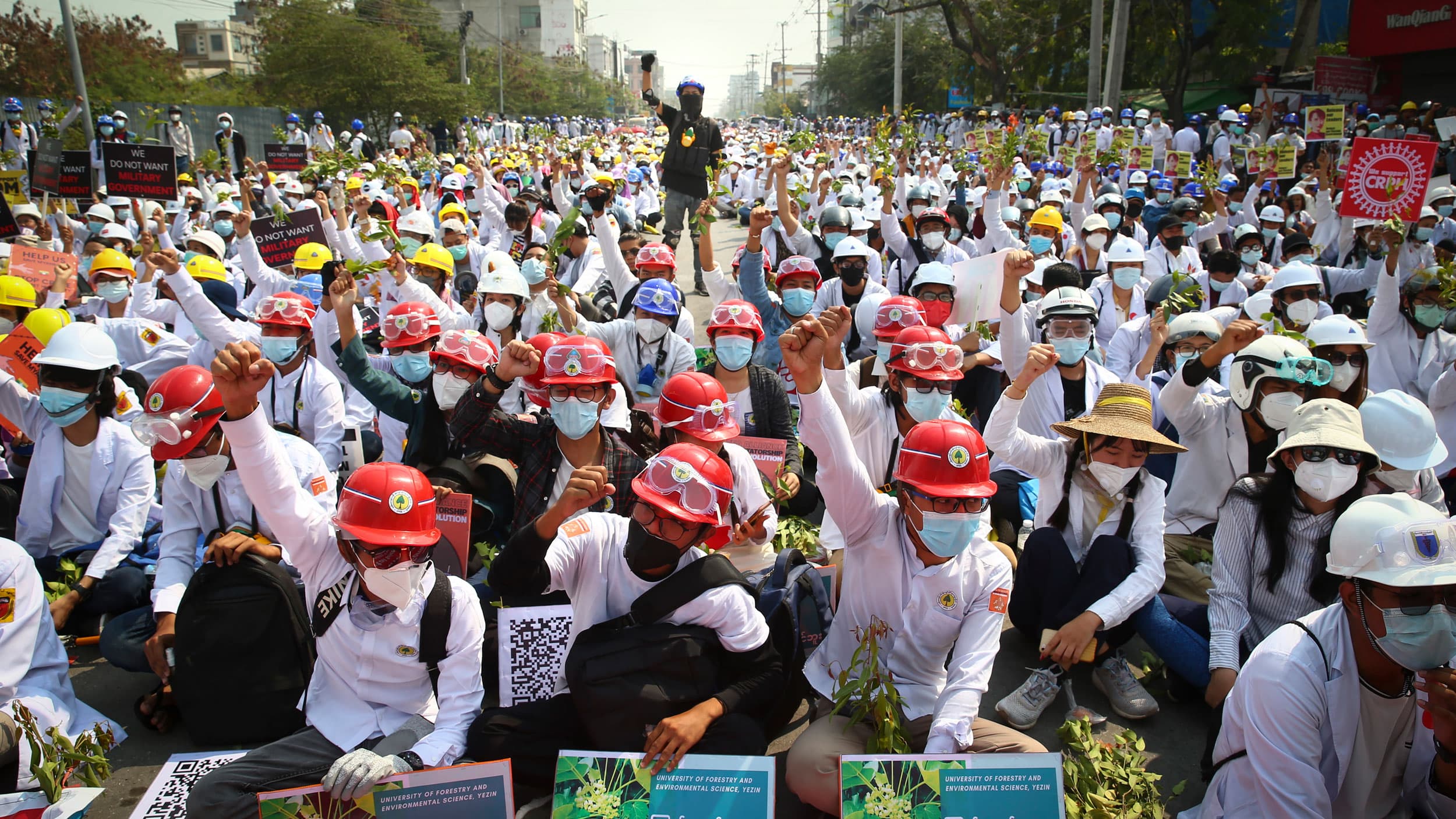 A large crowd of protesters are shown, many wearing construction hard hats and with their fist raised in the air.