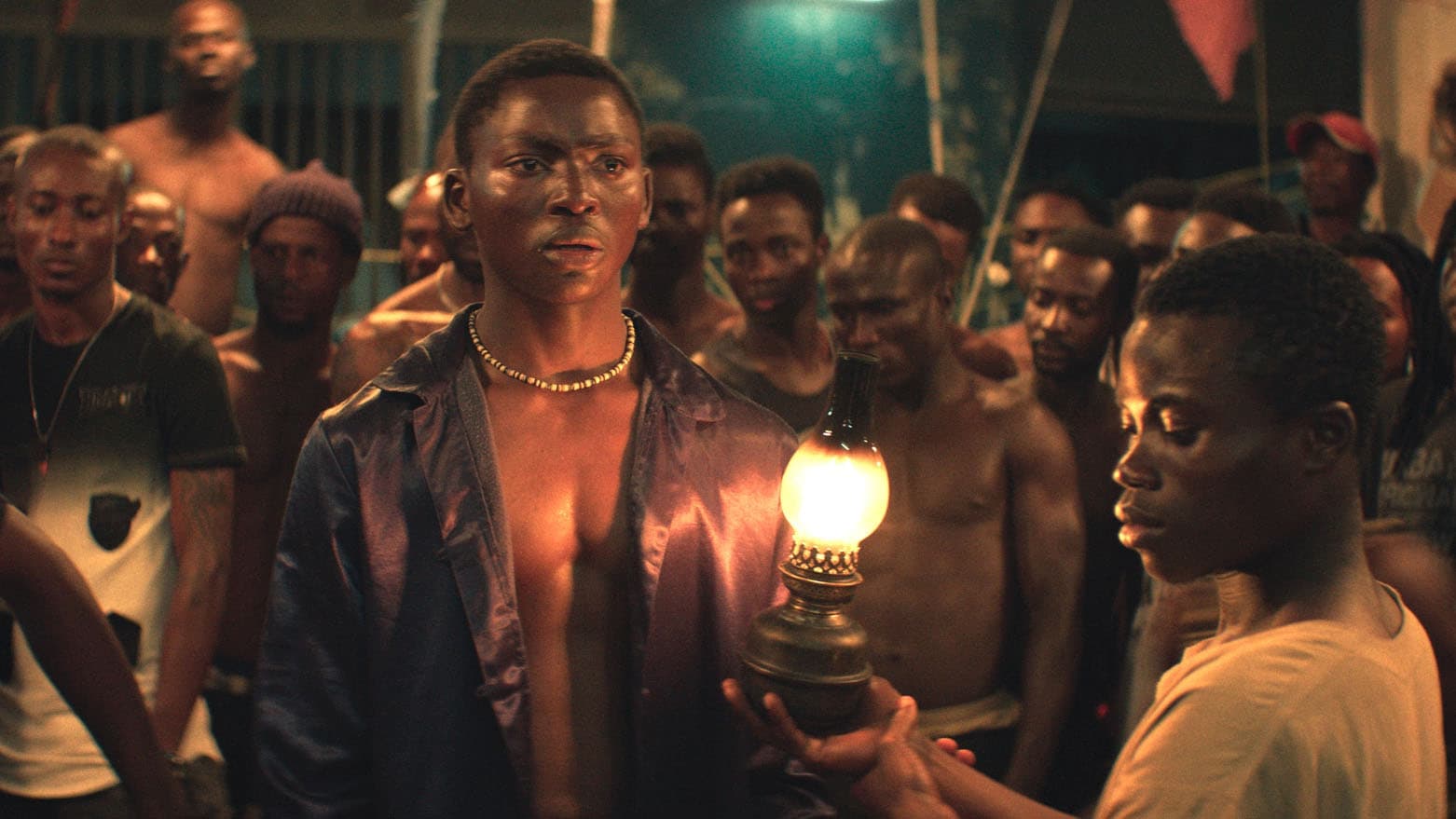 Two young Ivory Coast men stand in a crowded prison with a small lantern lit.