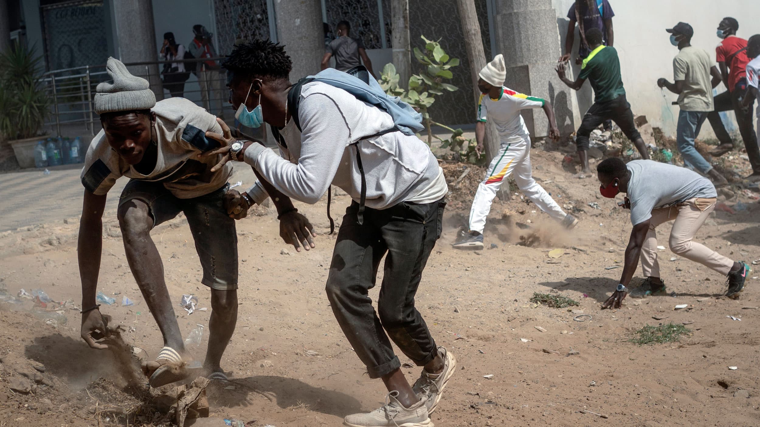 Several people are shown running and crouching down in a dirt road.