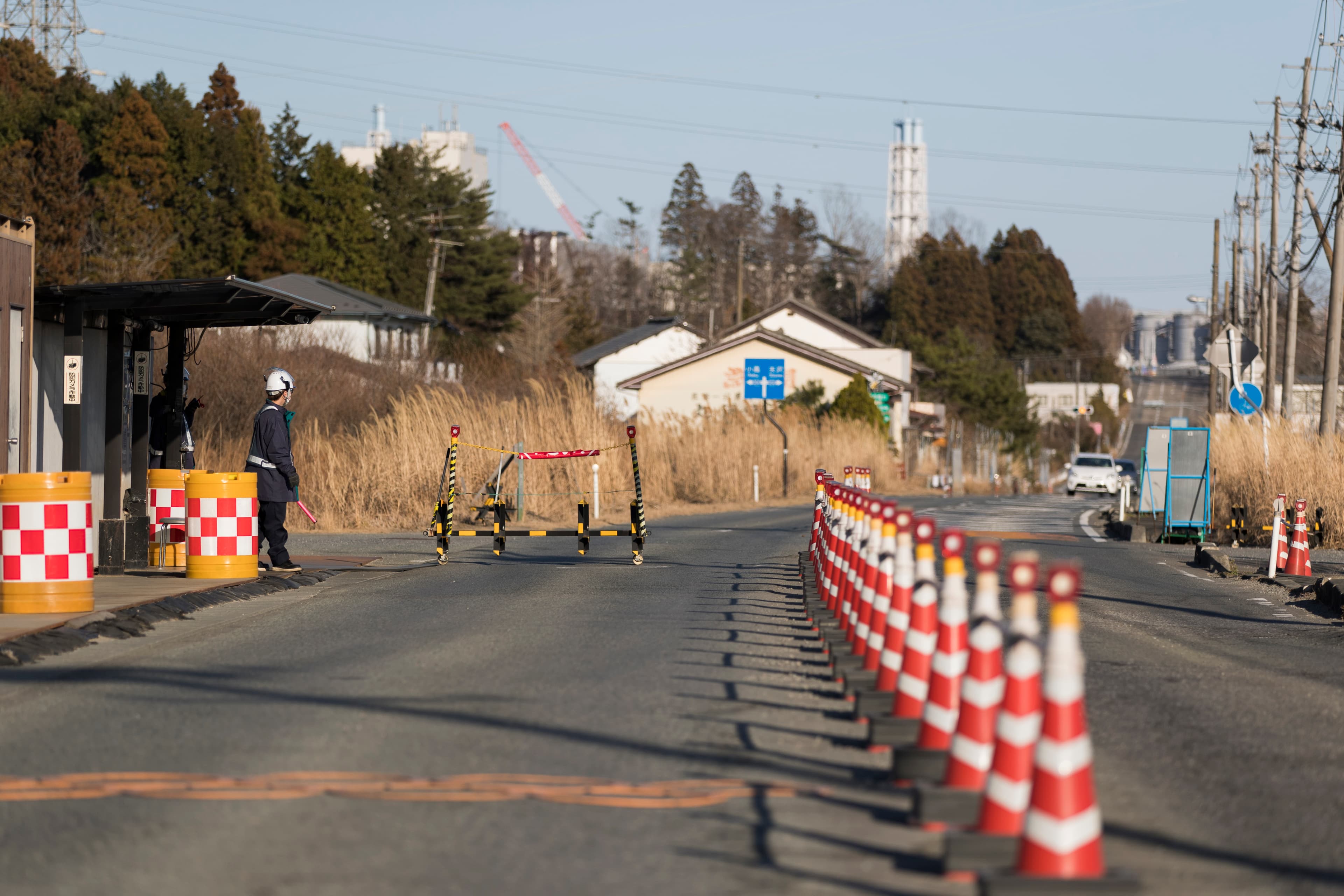 Security guards look at outbound vehicles moving toward them at a security checkpoint where part of the Fukushima Daiichi nuclear power plant is seen in the background in Okuma town in Fukushima prefecture, northeastern Japan, Feb. 25, 2021. An official