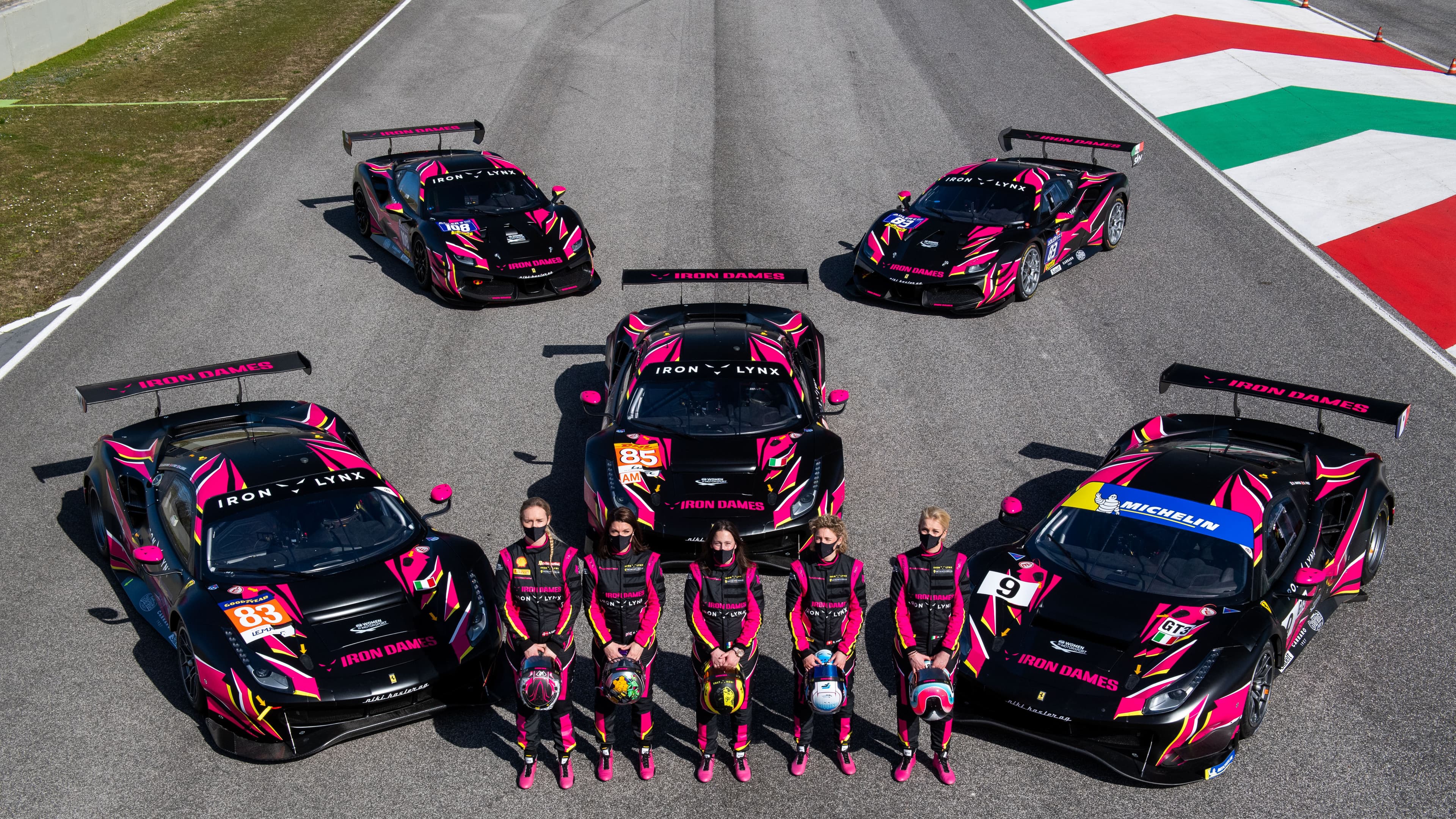 The Iron Dames line up in front of their race cars on the race track.