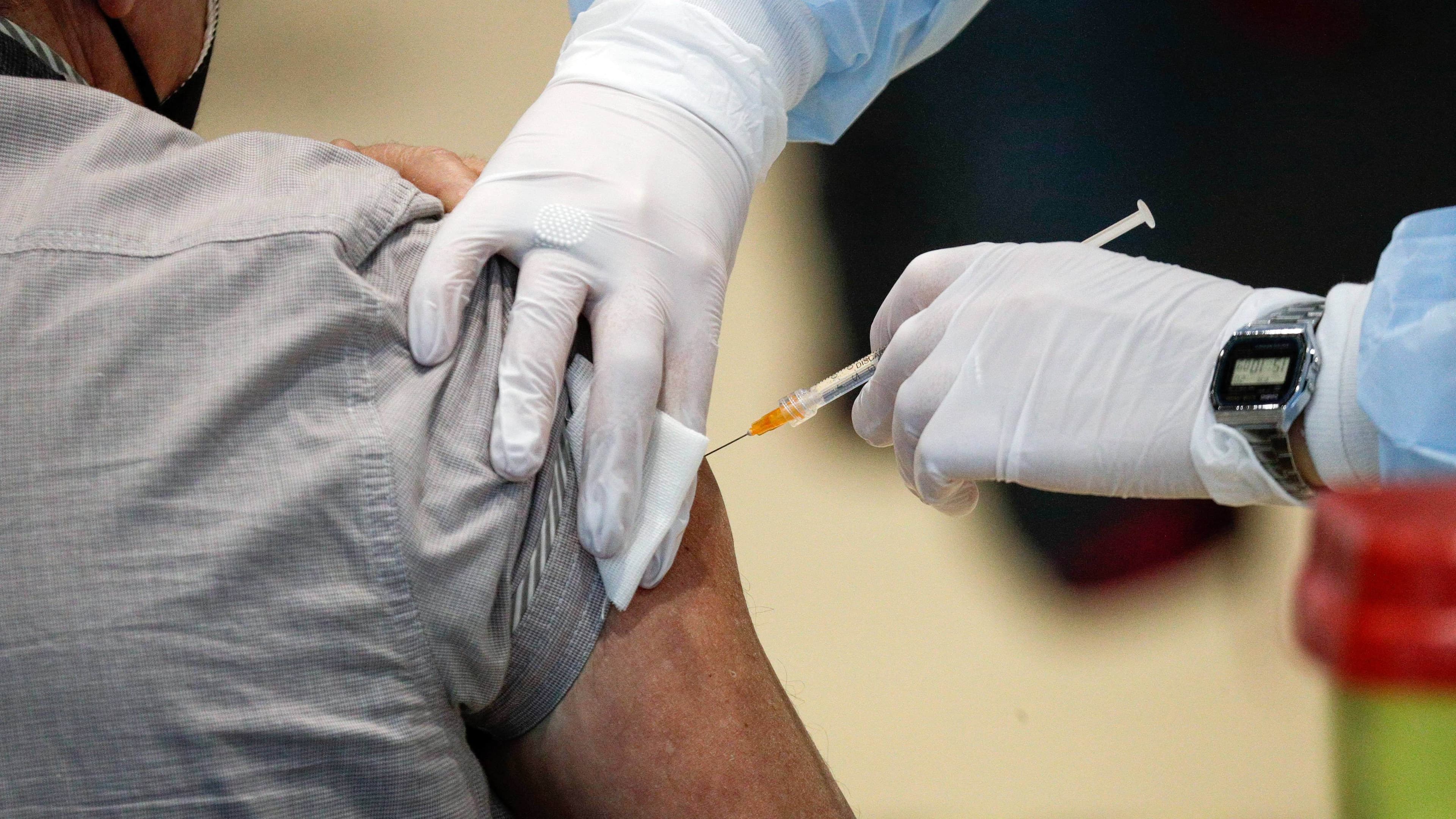 A person receives a jab from a health worker wearing white gloves