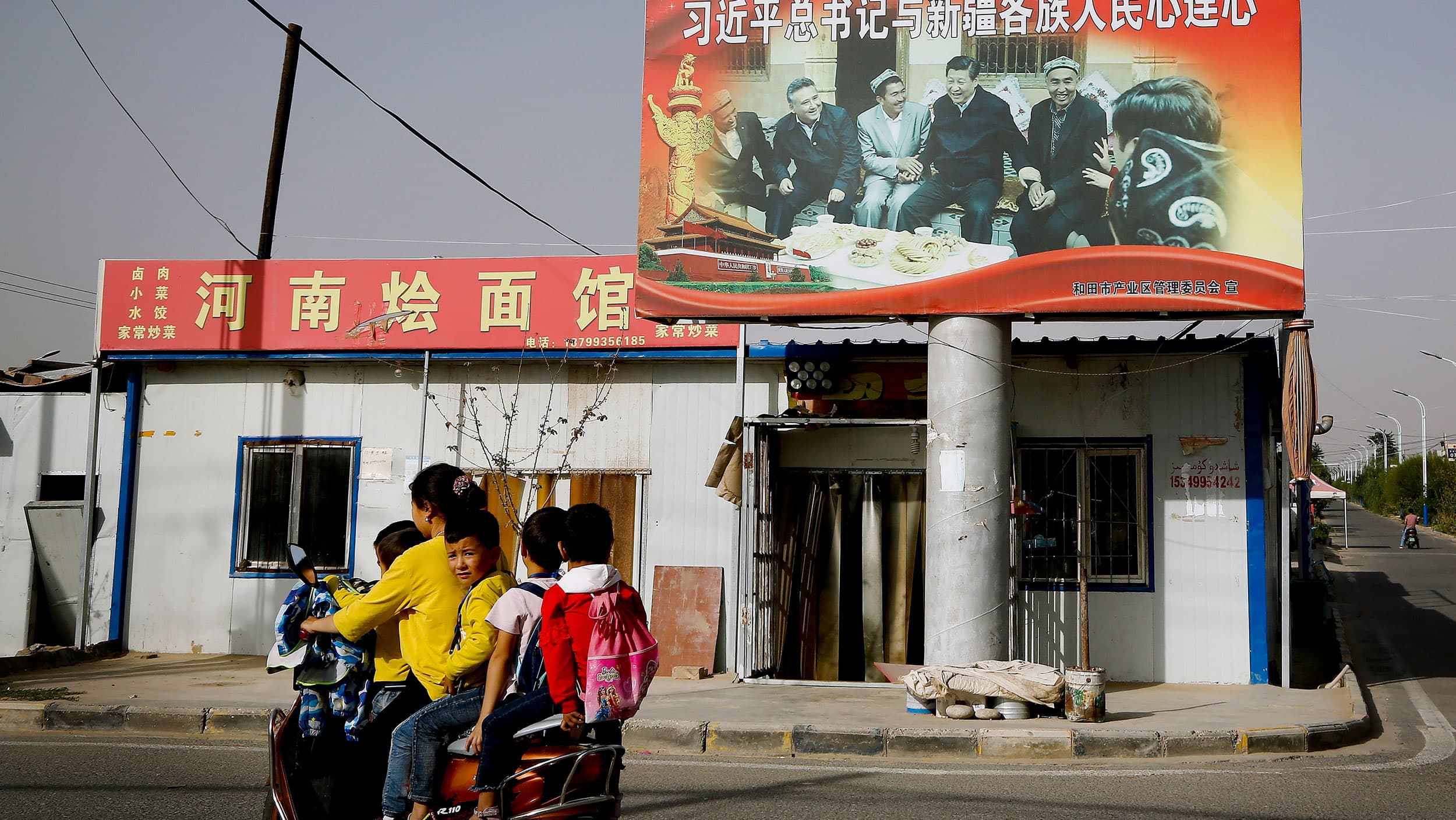 A woman is shown wearing a yellow jacket and driving a scooter with four children also onboard.