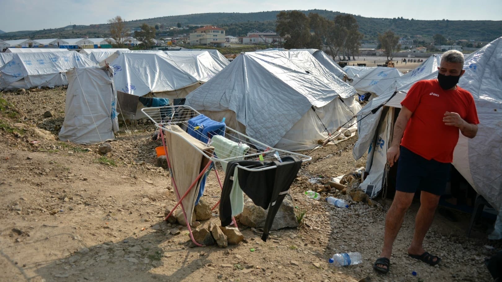 A migrant stands outside his tent at Karatepe refugee camp, on the northeastern Aegean island of Lesbos, Greece, March 29, 2021. The European Union's home affairs commissioner is visiting asylum-seeker facilities on the eastern Greek islands of Samos and