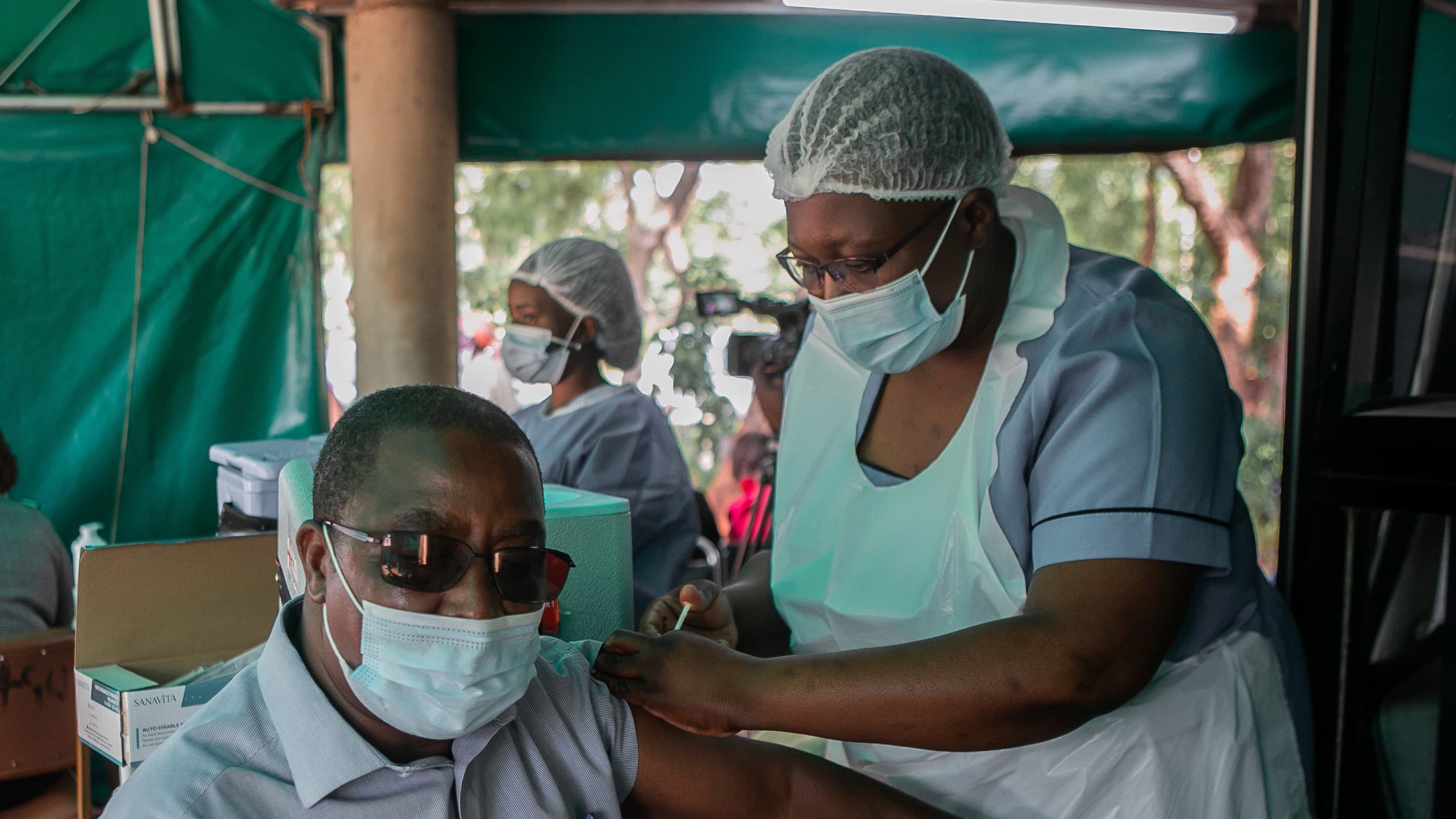 A man receives a shot from a health worker, both wear masks and protective gear.