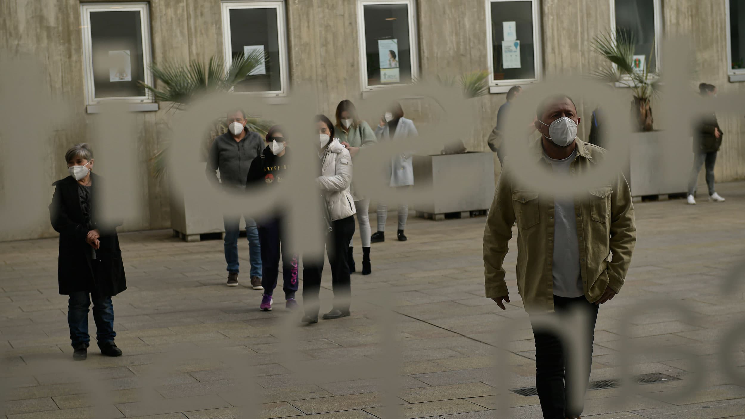 People are shown waiting in a line through a window with frosted lettering.