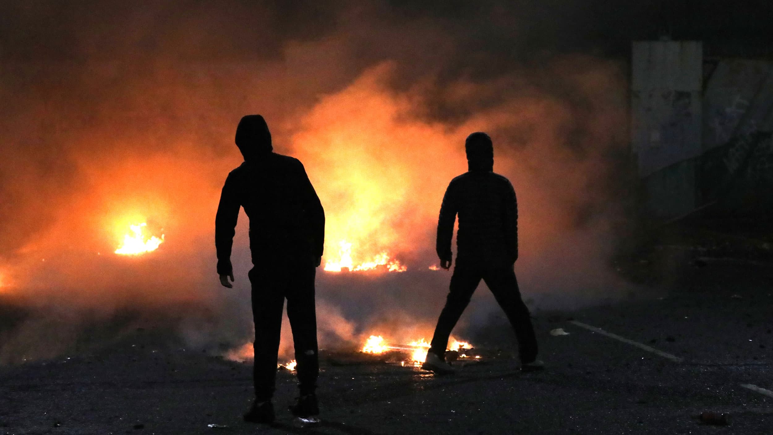Two people are shown in shadow with a large fire shown in the distance.