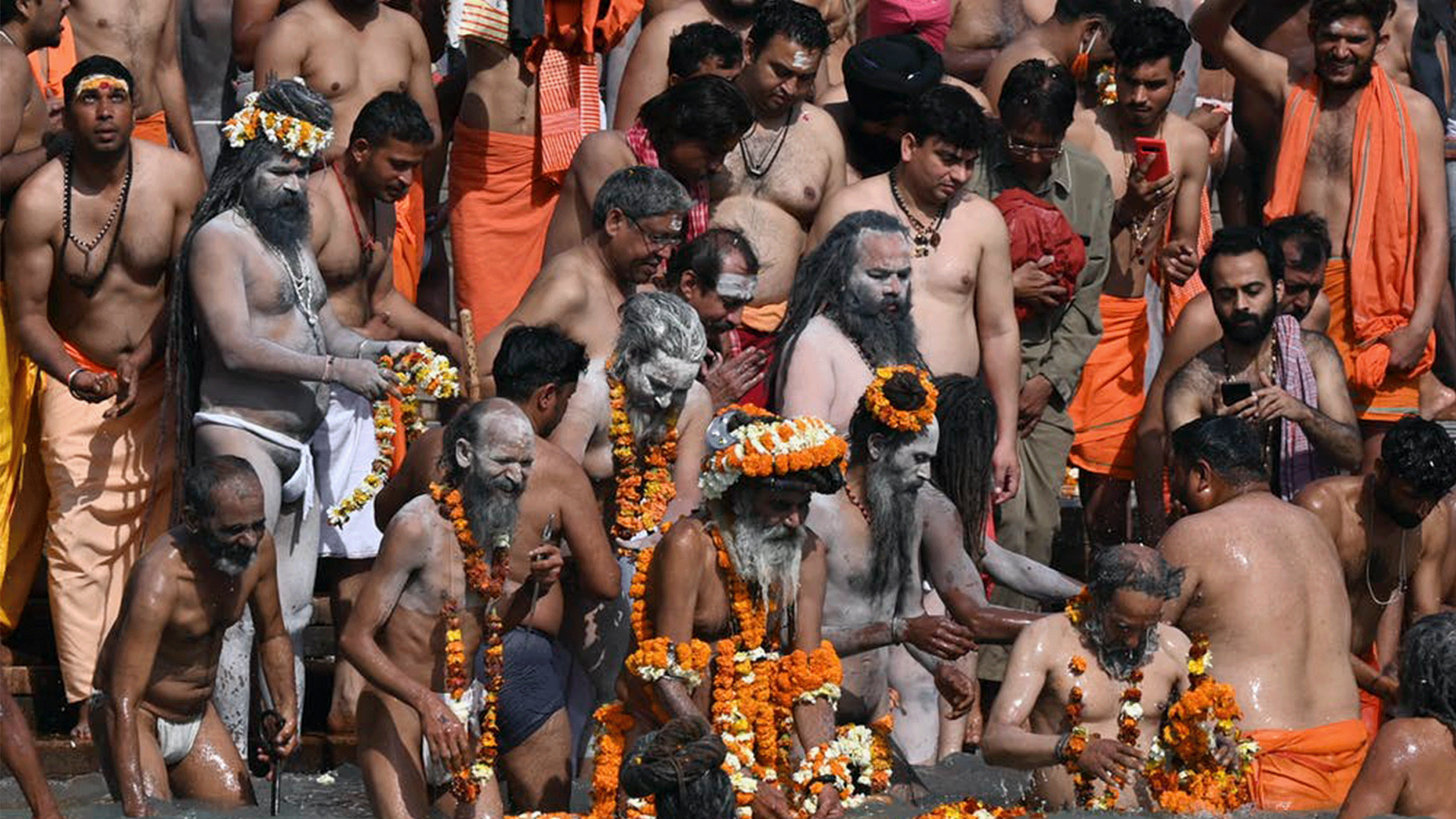 Men in orange cloth gather on the banks of a river