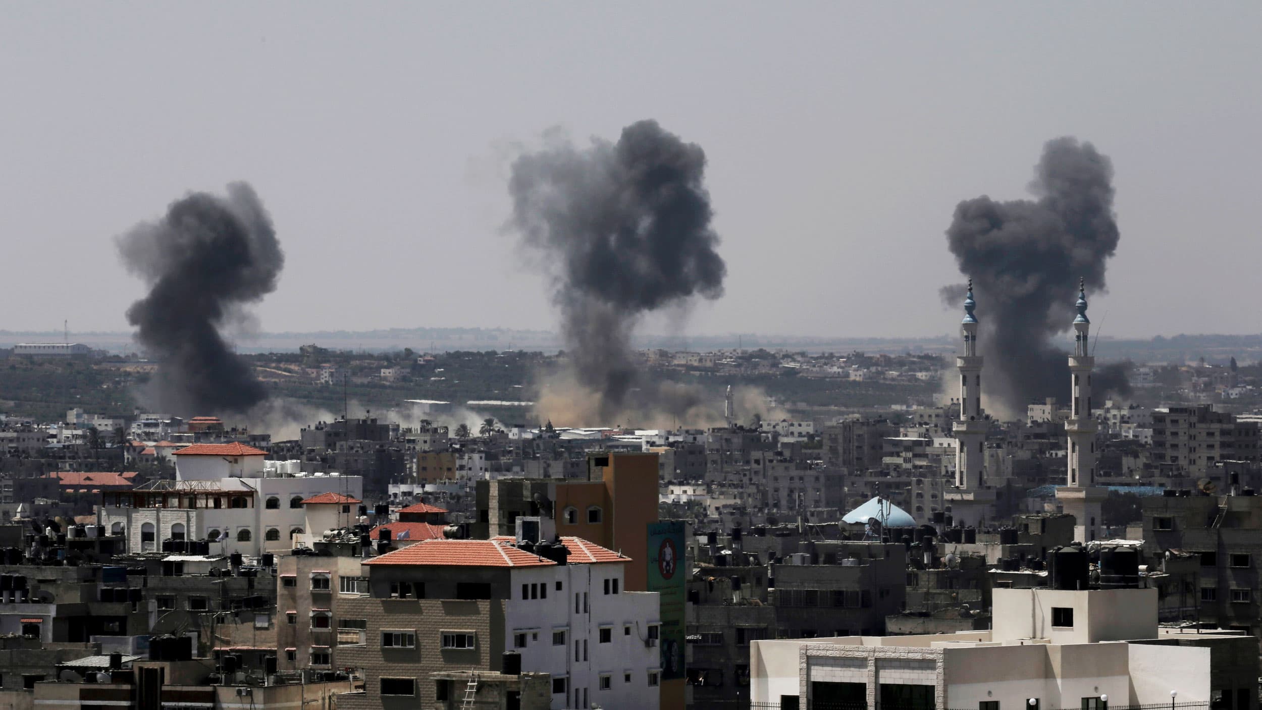 A city in the Gaza strip is show from afar with three clouds of black smoke rising.