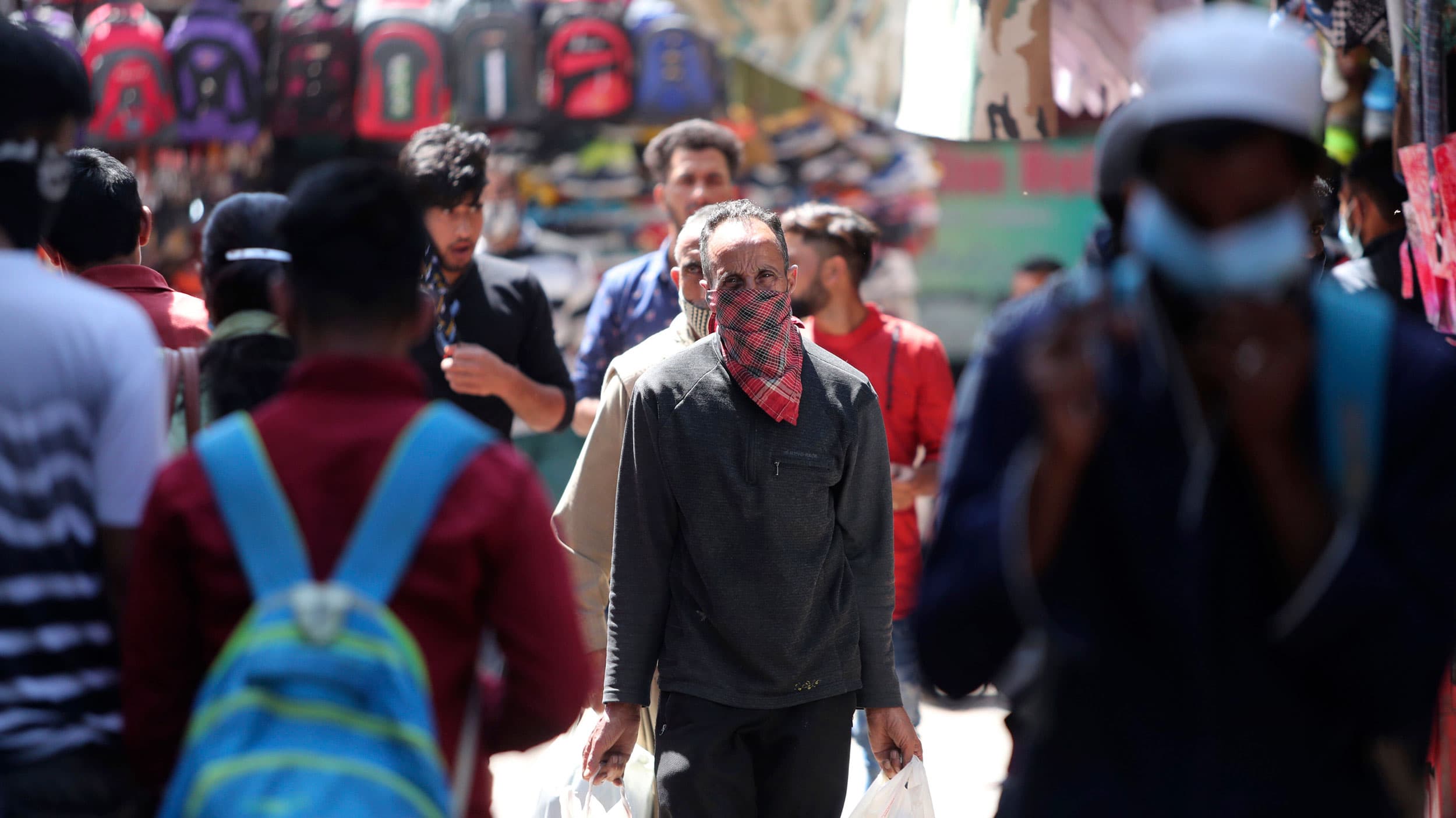 A crowd of people are shown in the street with one man in the center fram wearing a scarf over his face.