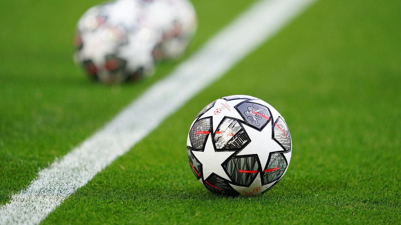 A soccer ball with stars on it rests on a green field near a white line and a soccer ball on the other side.