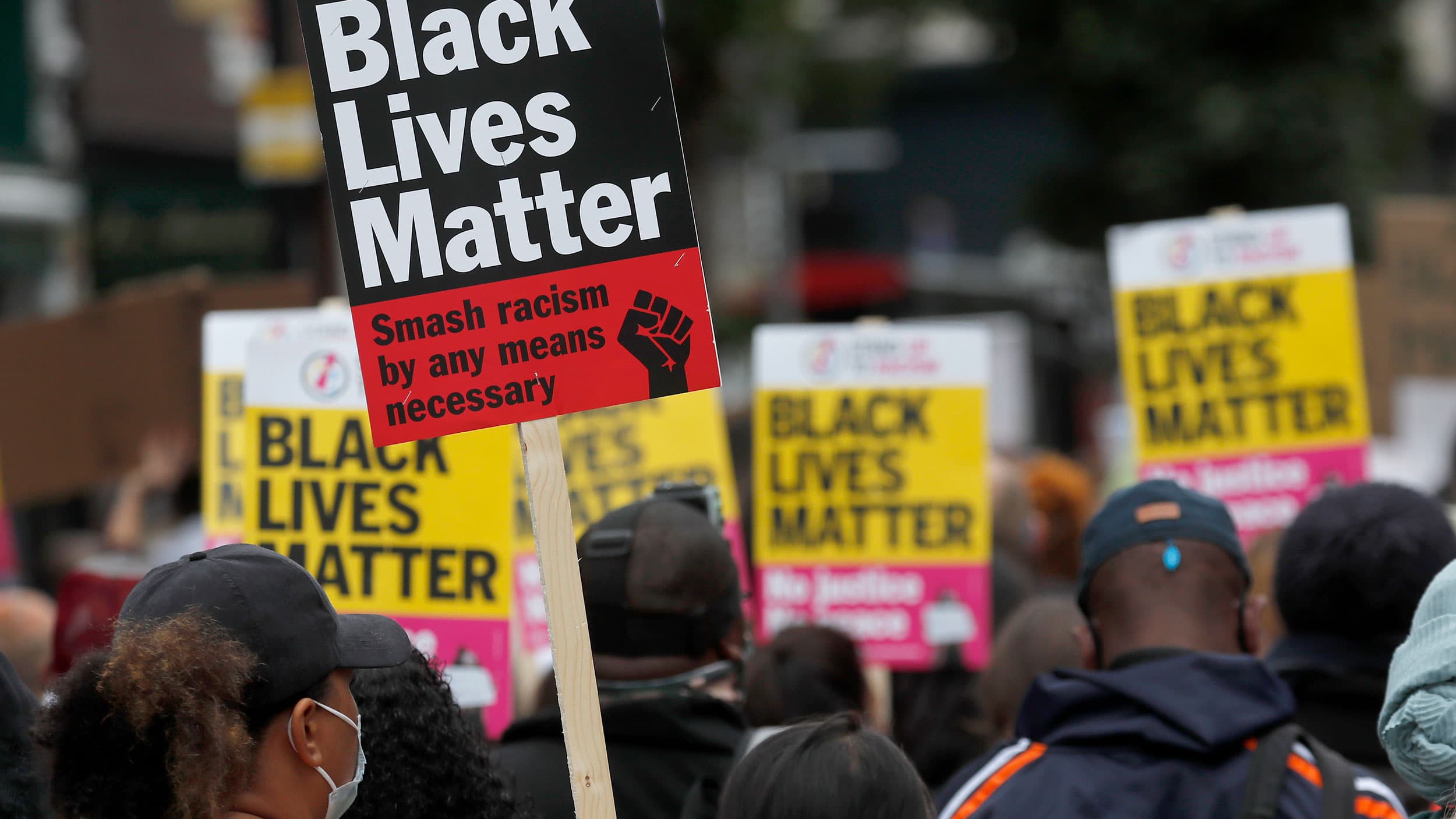 A large crowd of people are show, many holding yellow, red and black placards with Black Lives Matter printed on them.
