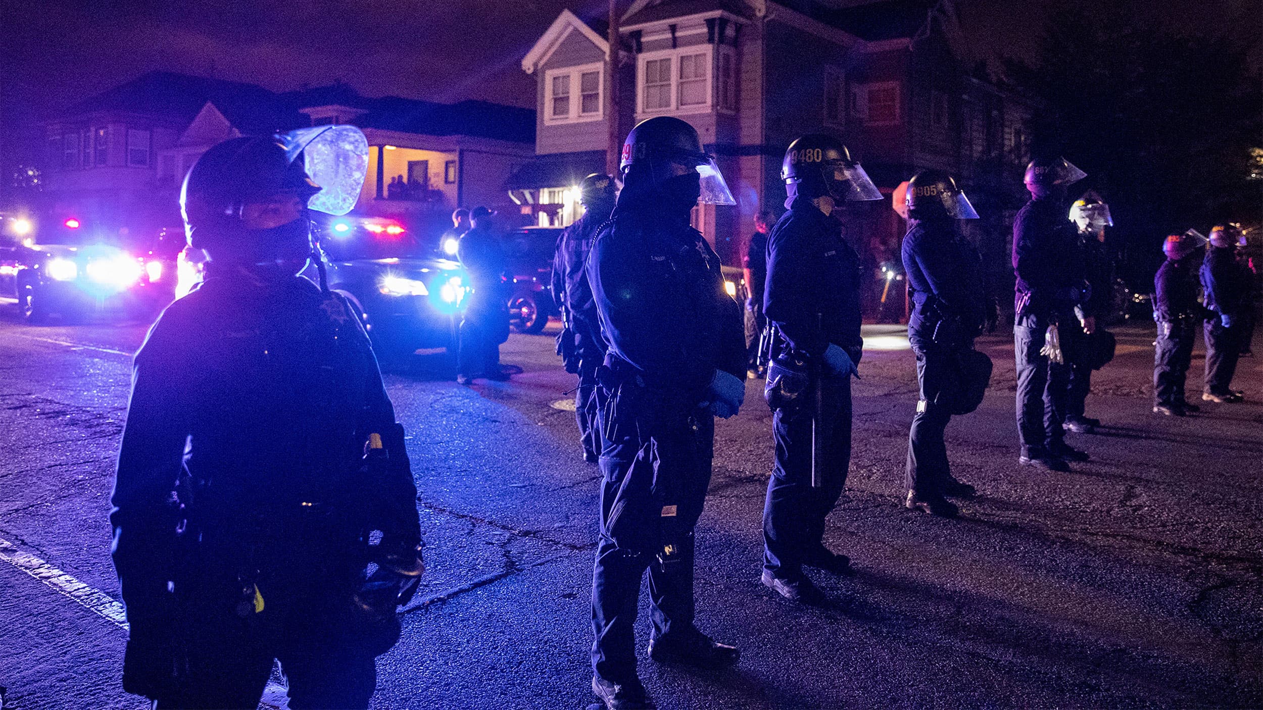 Police at night lining the street with police cars in the background with their lights on