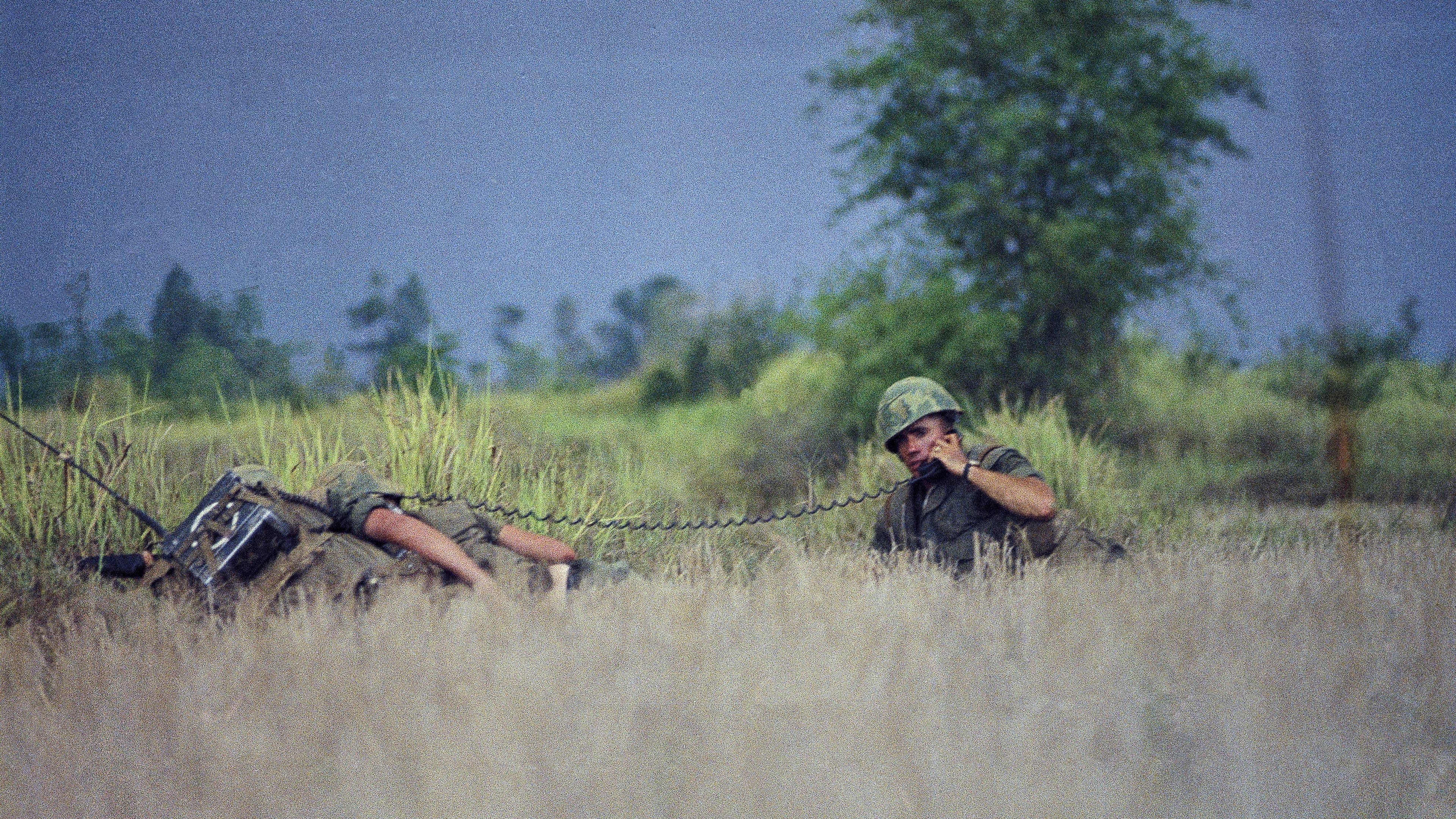 Two men in camouflage carry guns in a rice paddy in Vietnam.