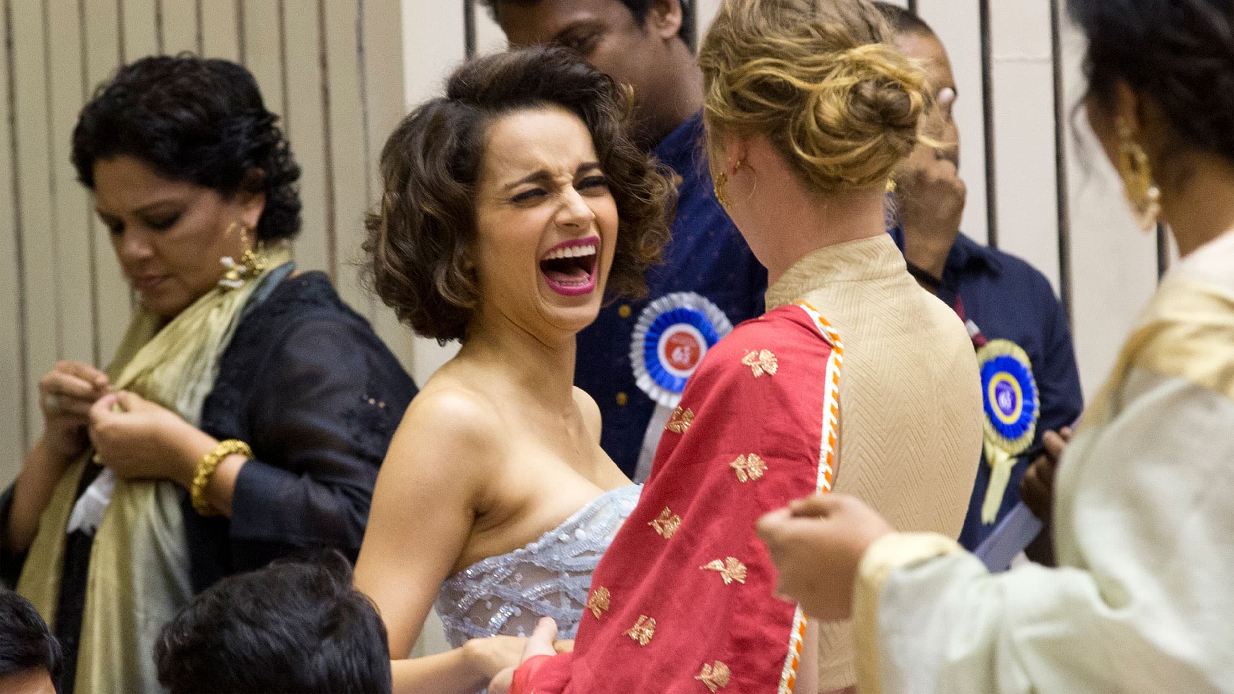 Woman in white dress laughs while talking to woman facing away from camera in red dress