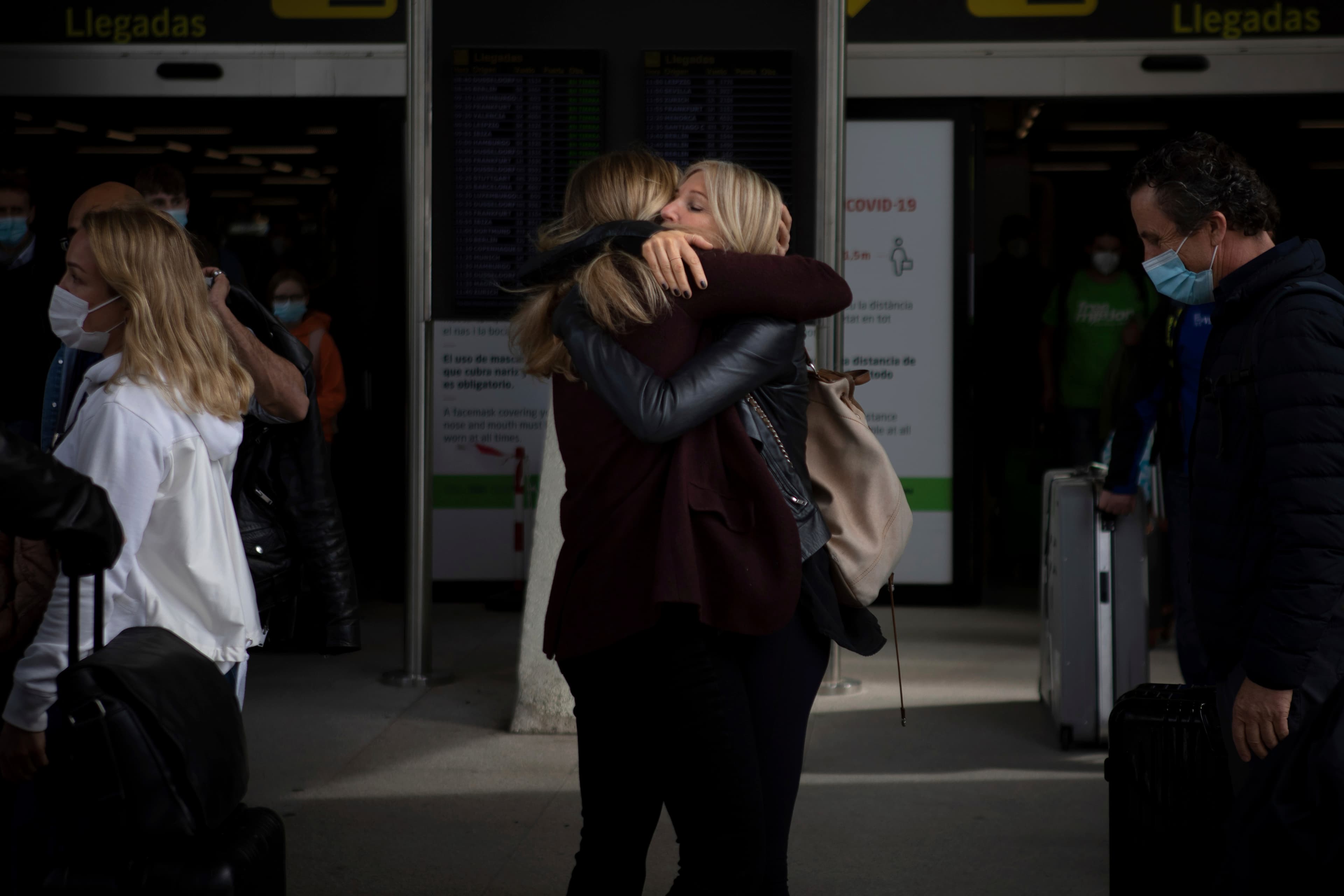 Two women in black clothing embrace in an airport