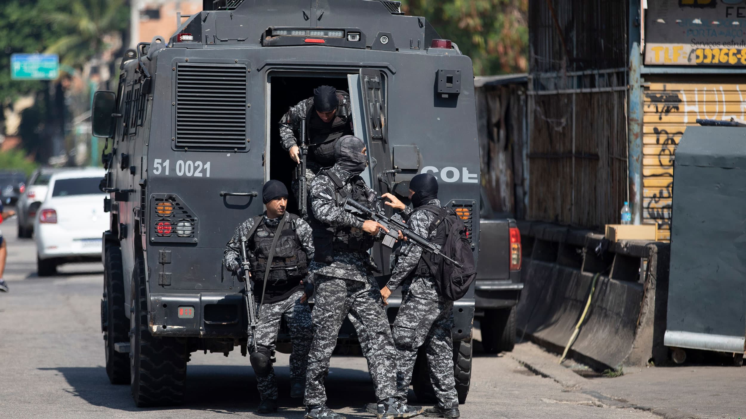 Several police officers are shown wearing dark colored fatigues and climbing out of a black armored vehicle carrying weapons.