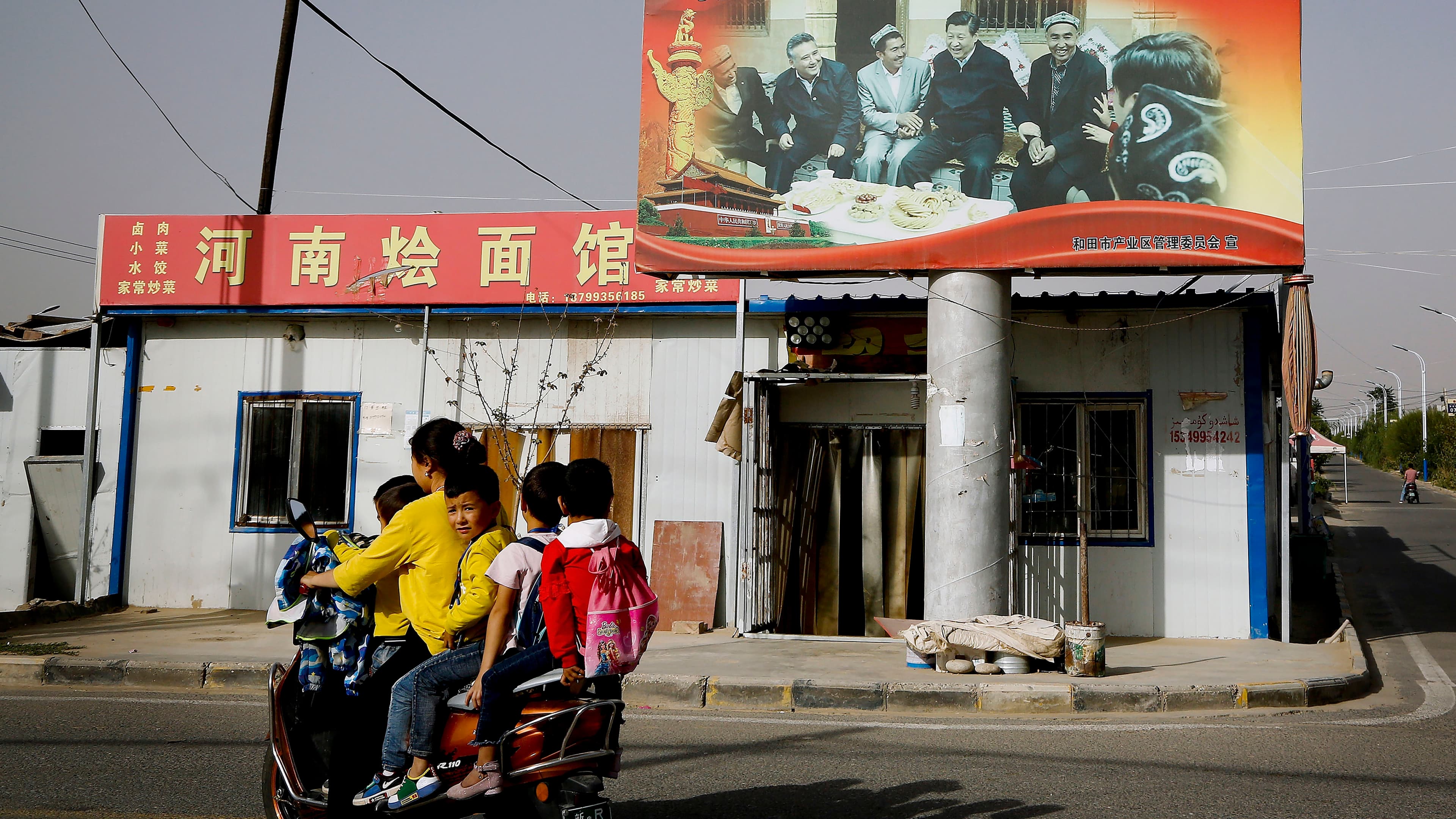 Children ride on a motorcycle near a large billboard.