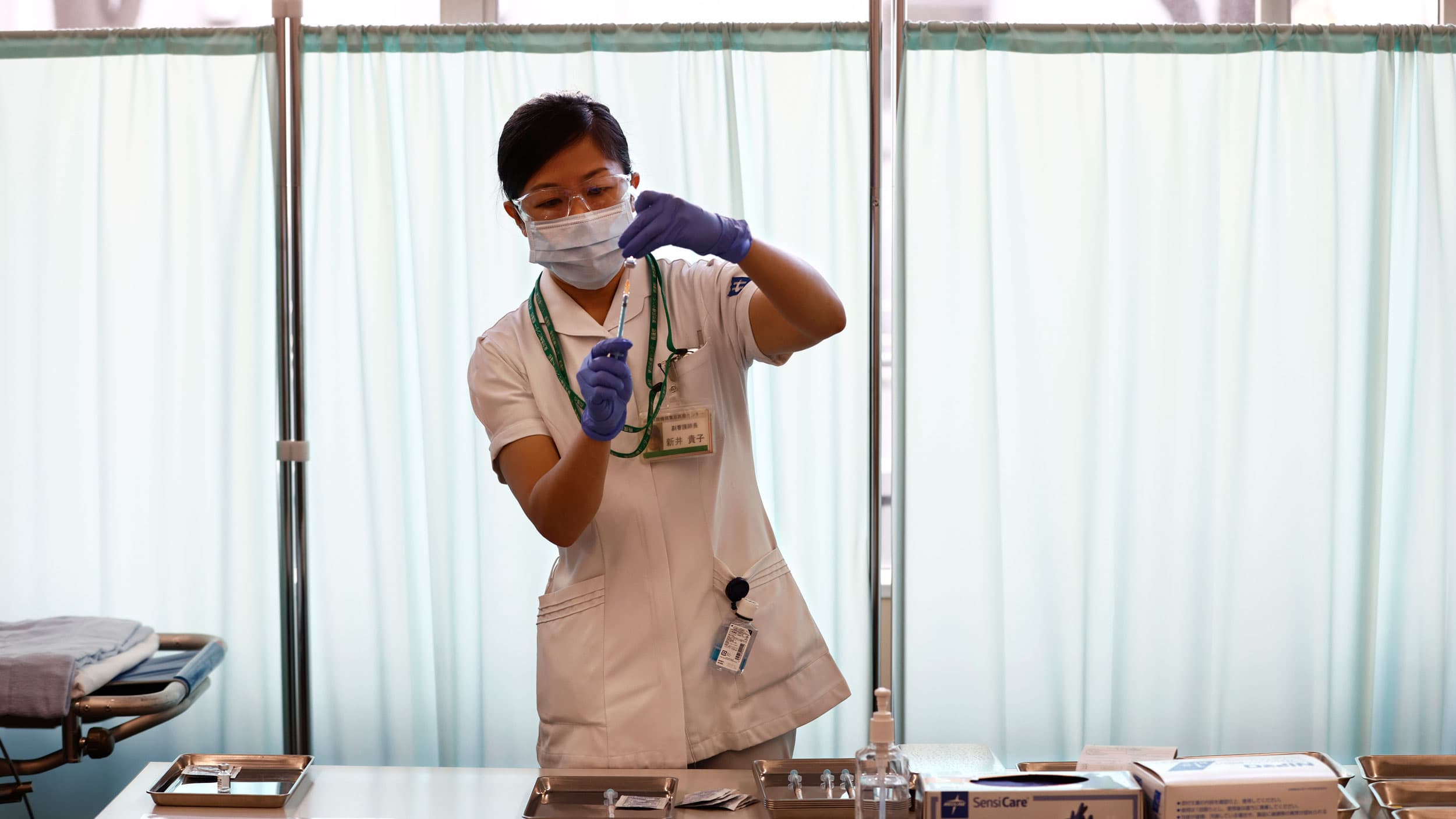 A medical worker is shown in white and blue latex gloves while filling a syringe with a vaccine.