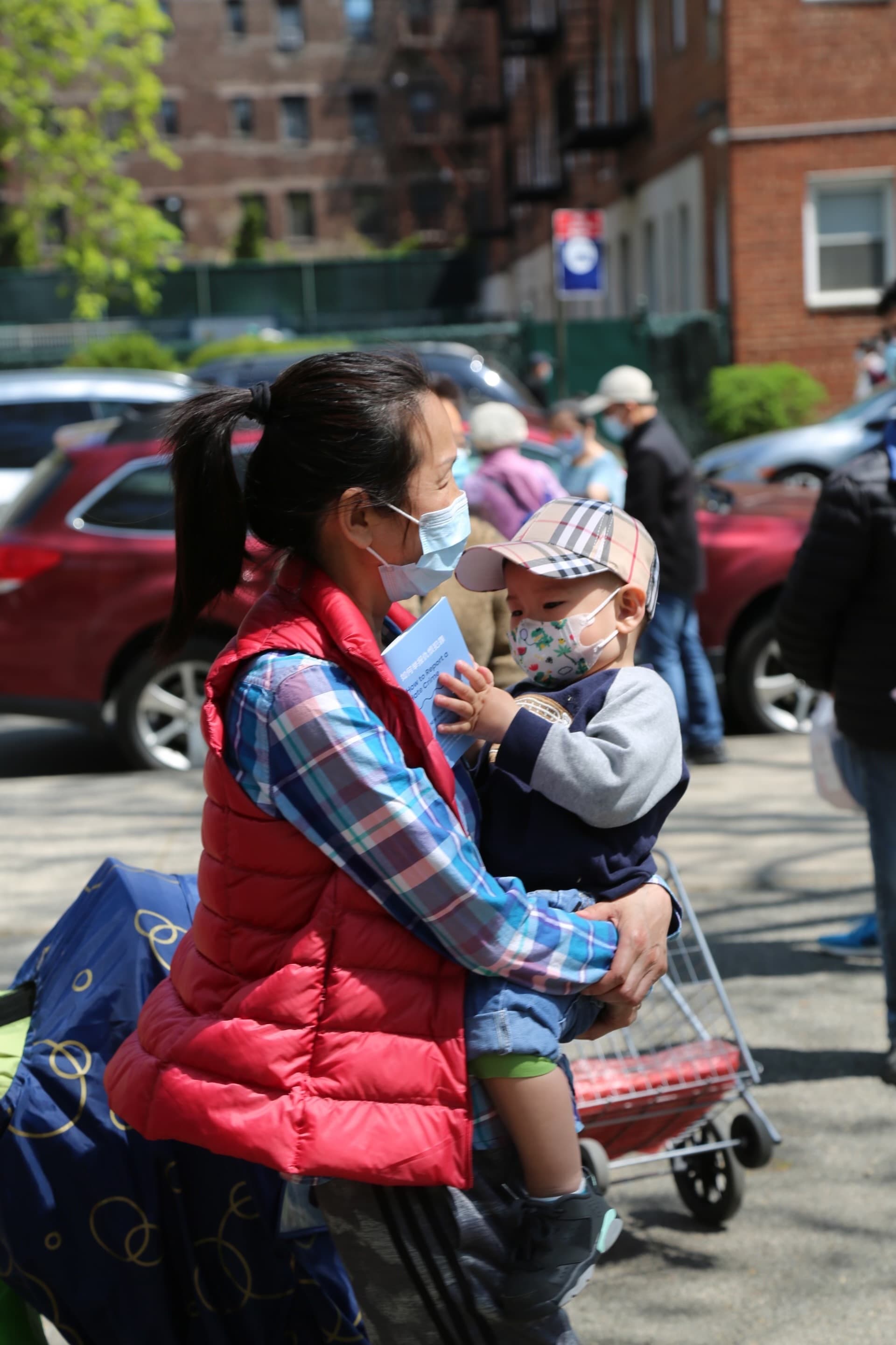 Woman wearing blue and red carries a child who is flipping through a booklet on 