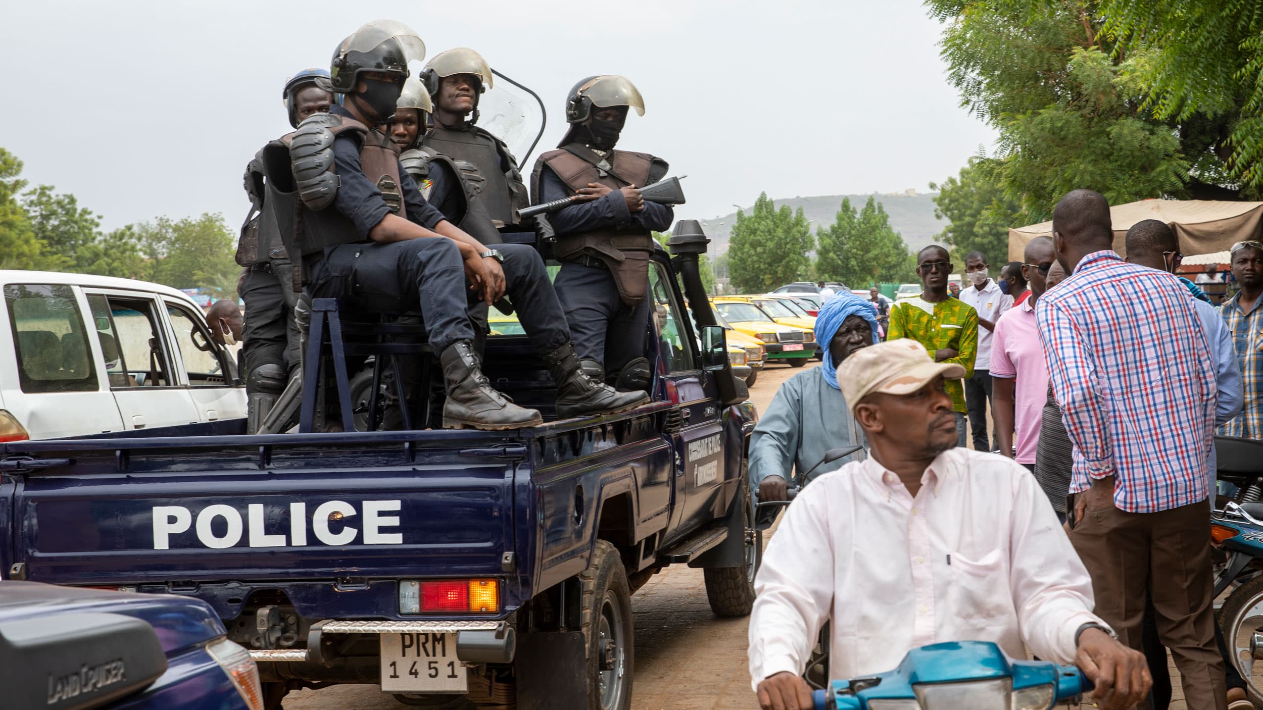 A crowd of people are shown next to a pickup truck with "Police" printed on the tail and several police officials standing in the bed of the truck.