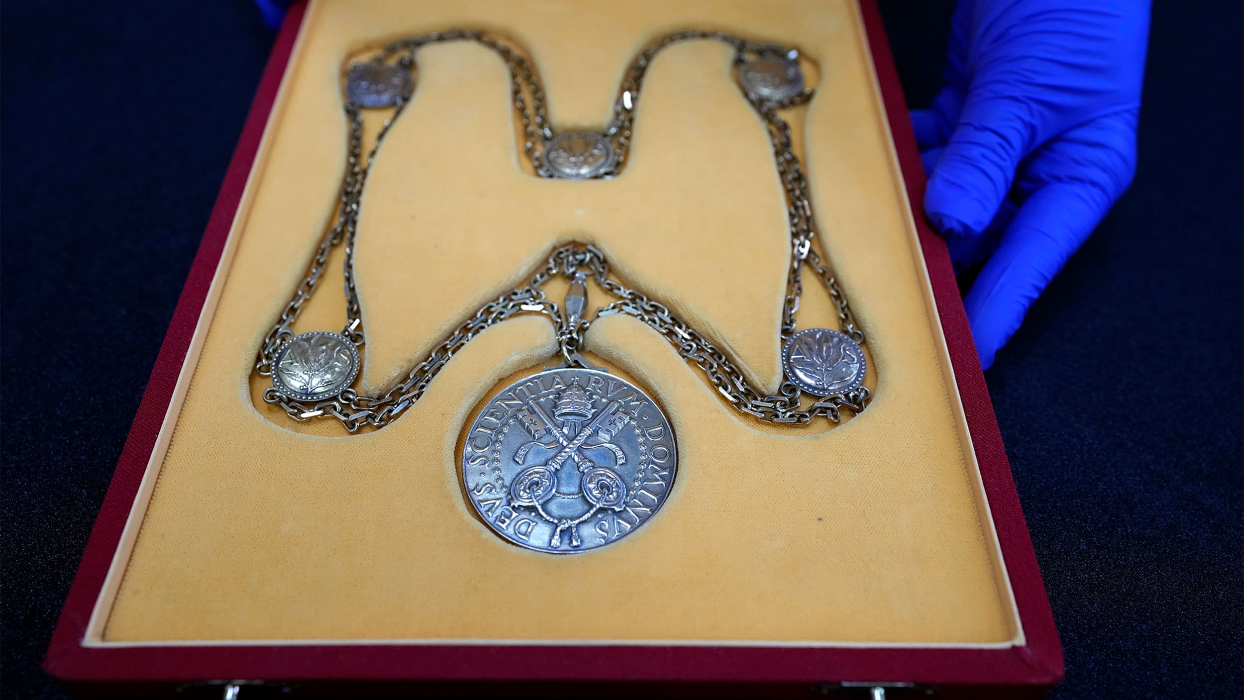 Person with blue gloves presents a large medal in a yellow and red box