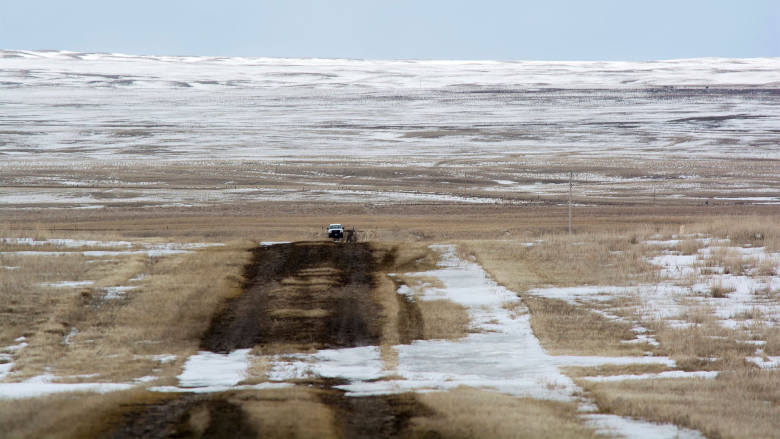 Wide shot of snowy barren land with a white car parked in the middle