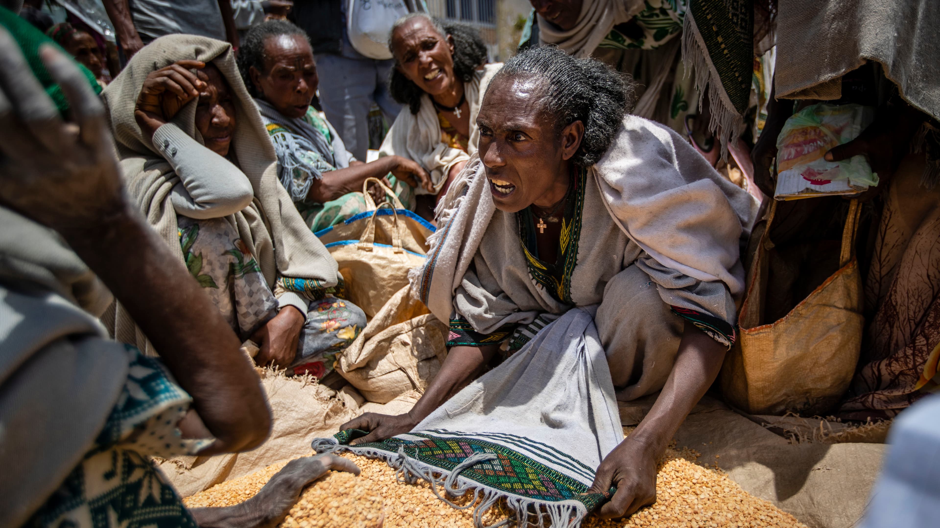 A woman argues over a pile of yellow lentils at a market.