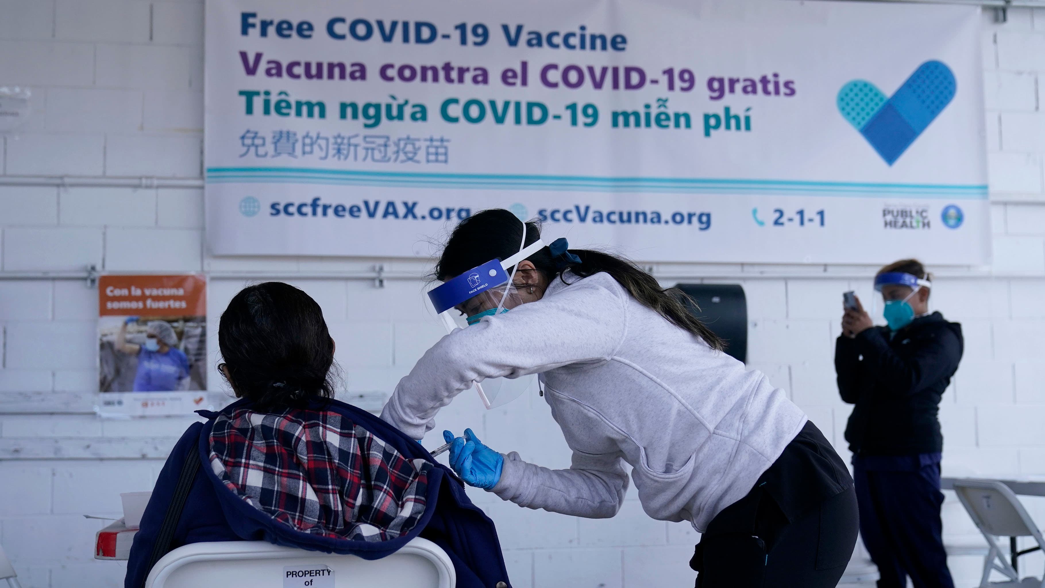 A member of the National Guard, center, administers the Moderna COVID-19 vaccine to a farmworker.