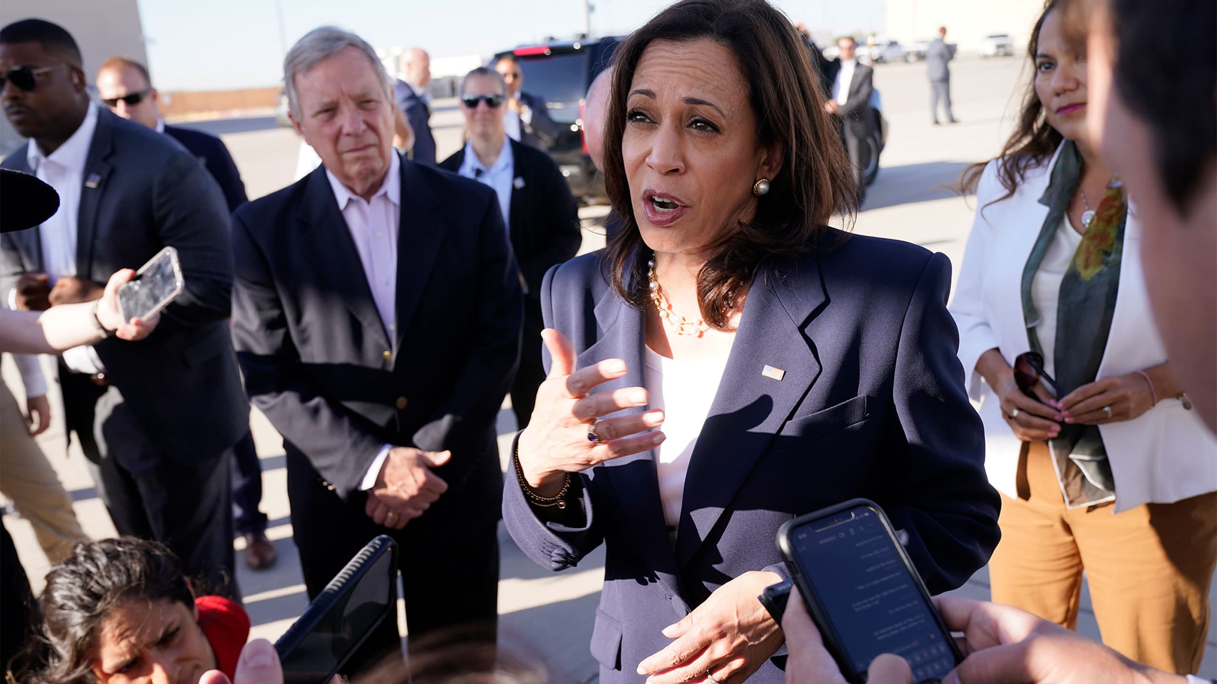 Vice president Kamala Harris, in a blue suit, speaks to reporters