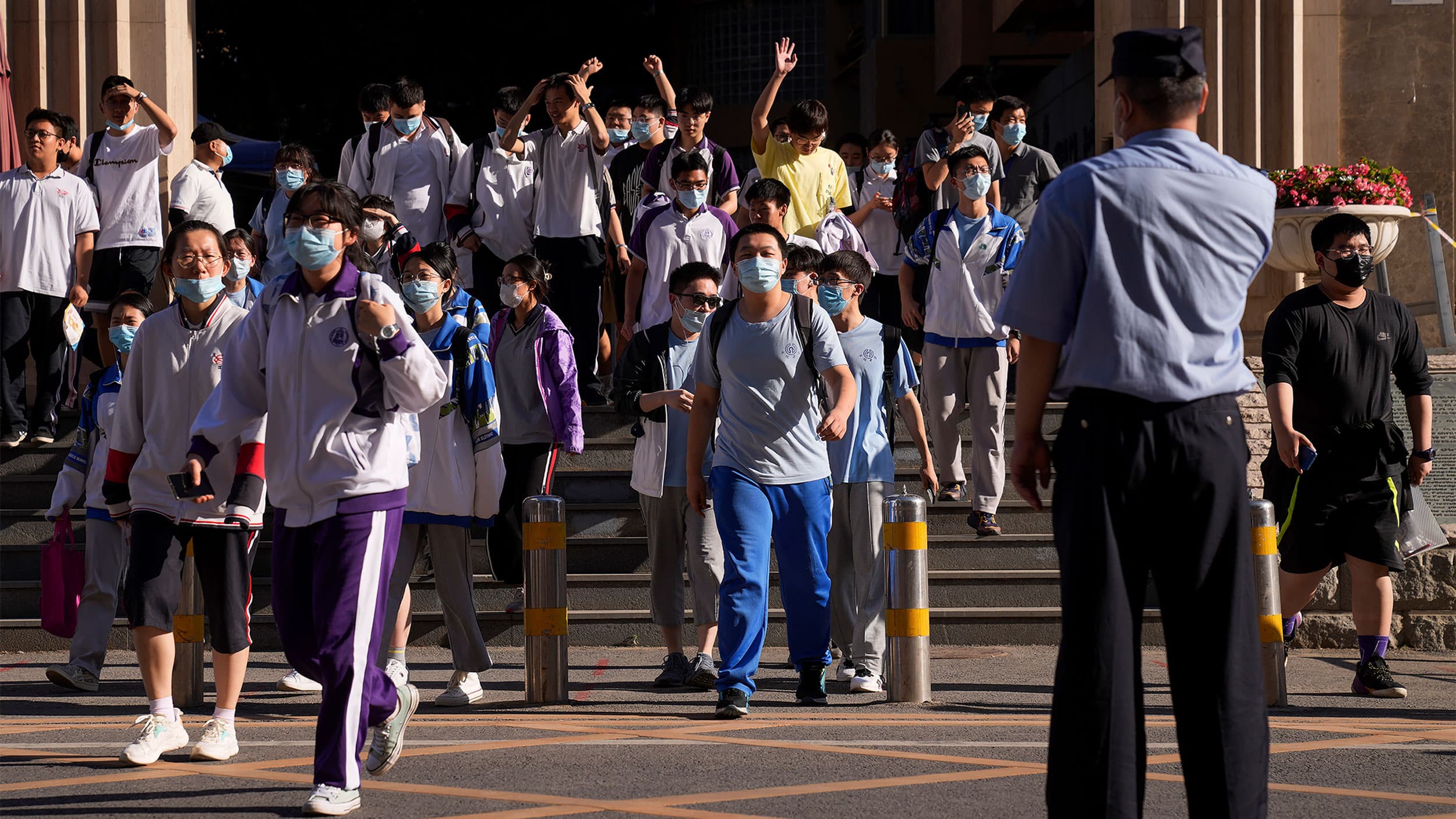 Students come out of a building, some with their hands in the air from relief, as a police officer looks on