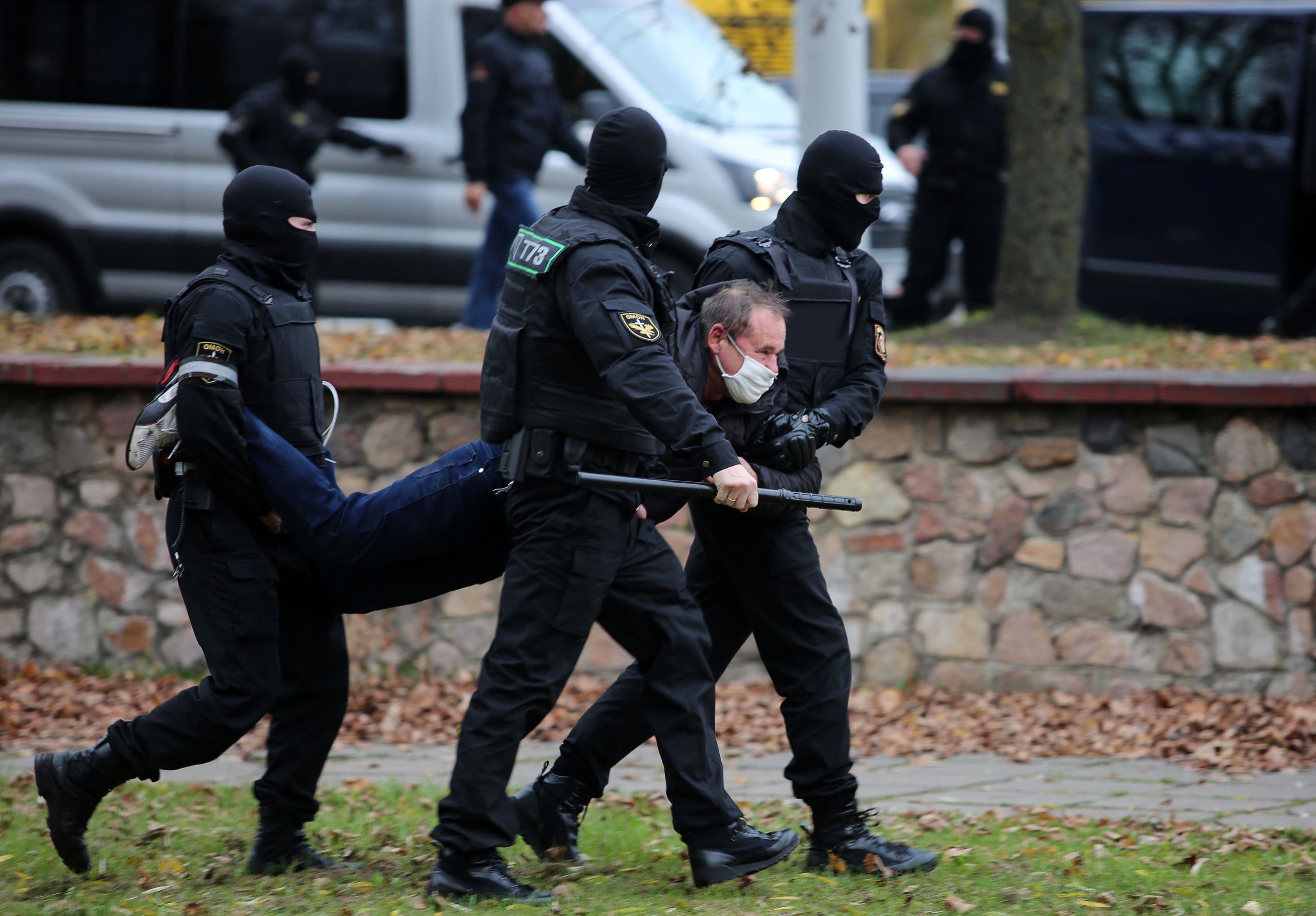 Three police officers in uniform carry a man by his arms and legs.