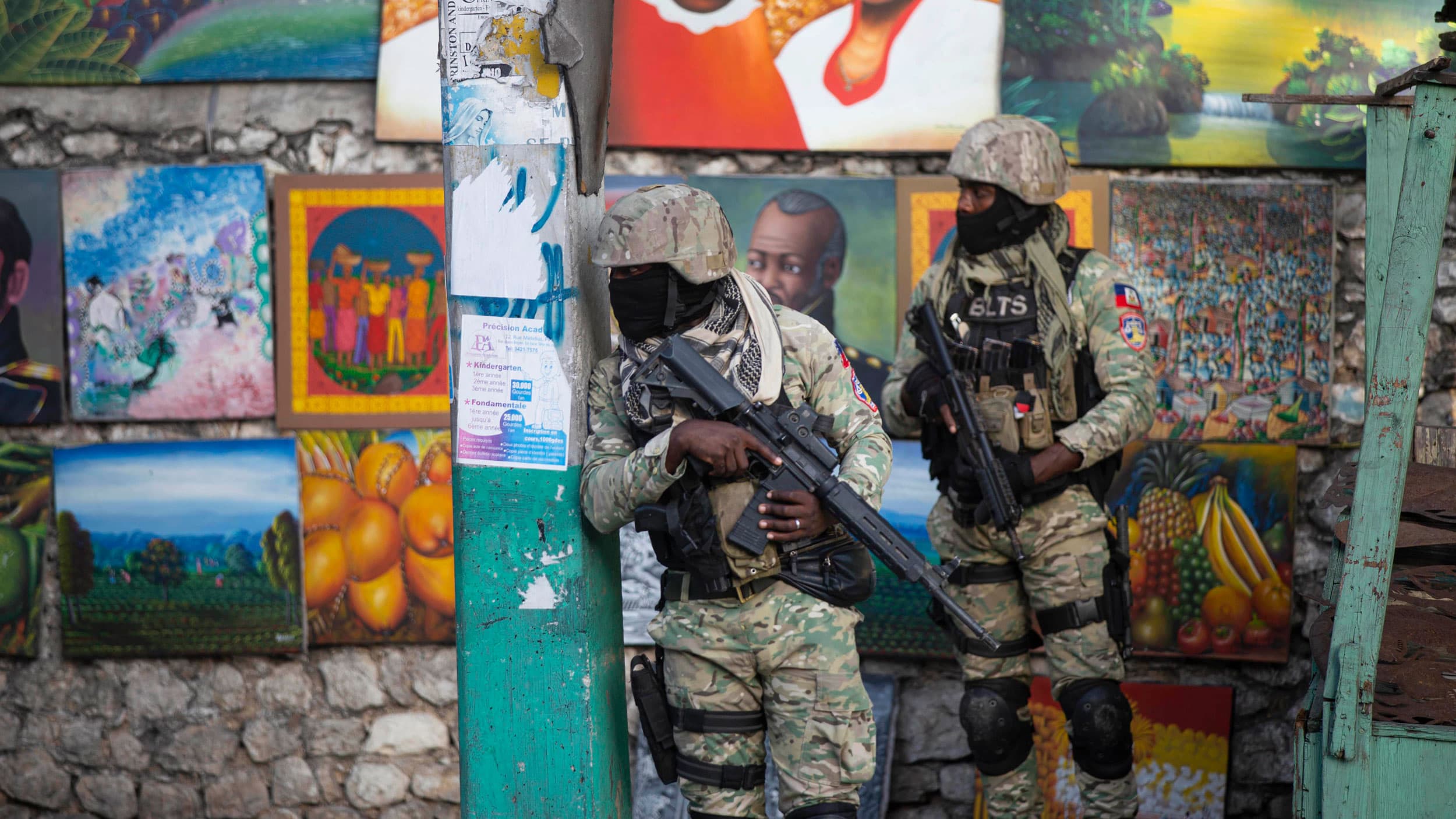 Two military personnel are shown wearing fatigues, black masks and carrying large rifles.