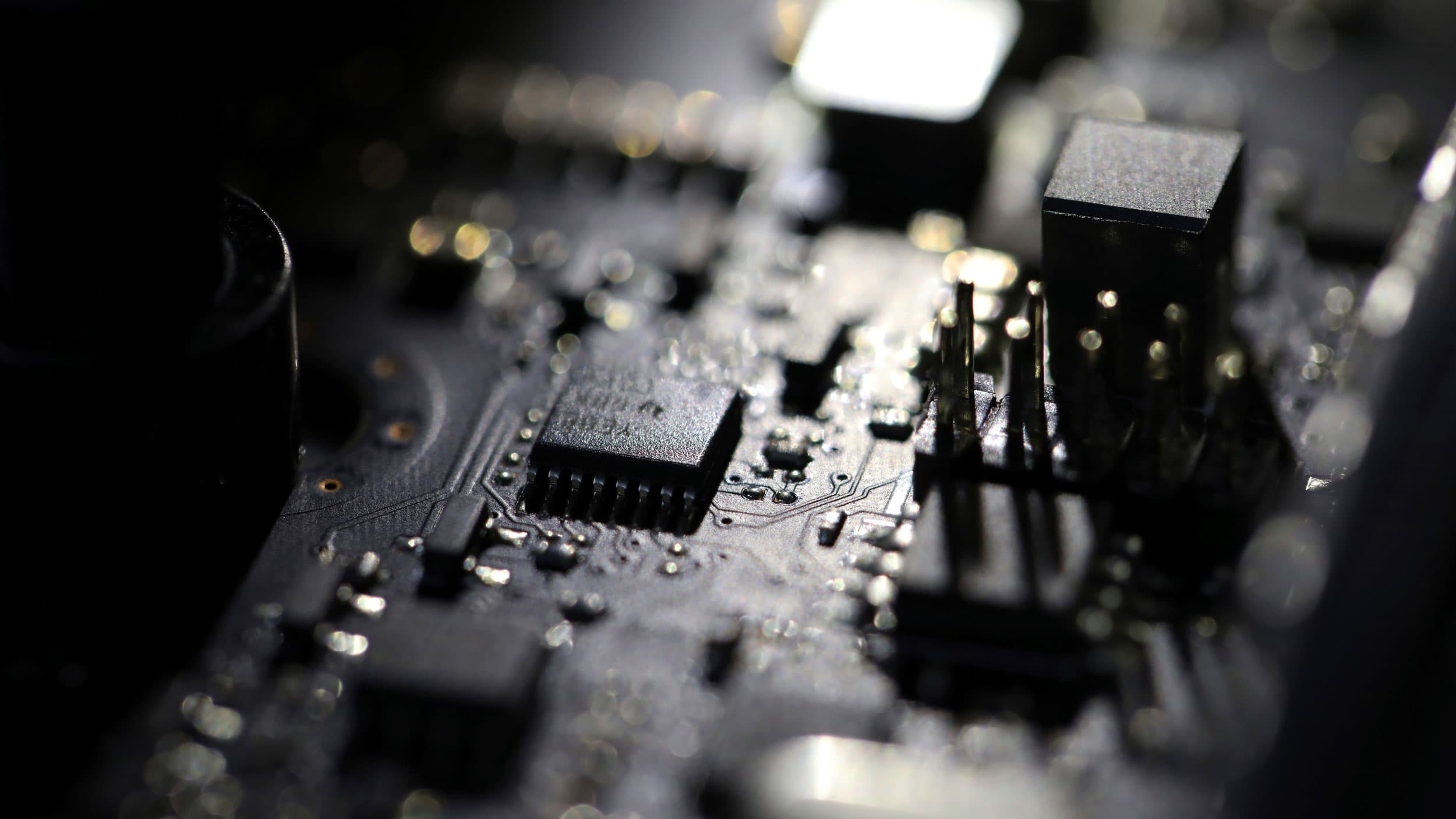 A close up photograph of a computer motherboard with circuits and microchips in high contrast light.