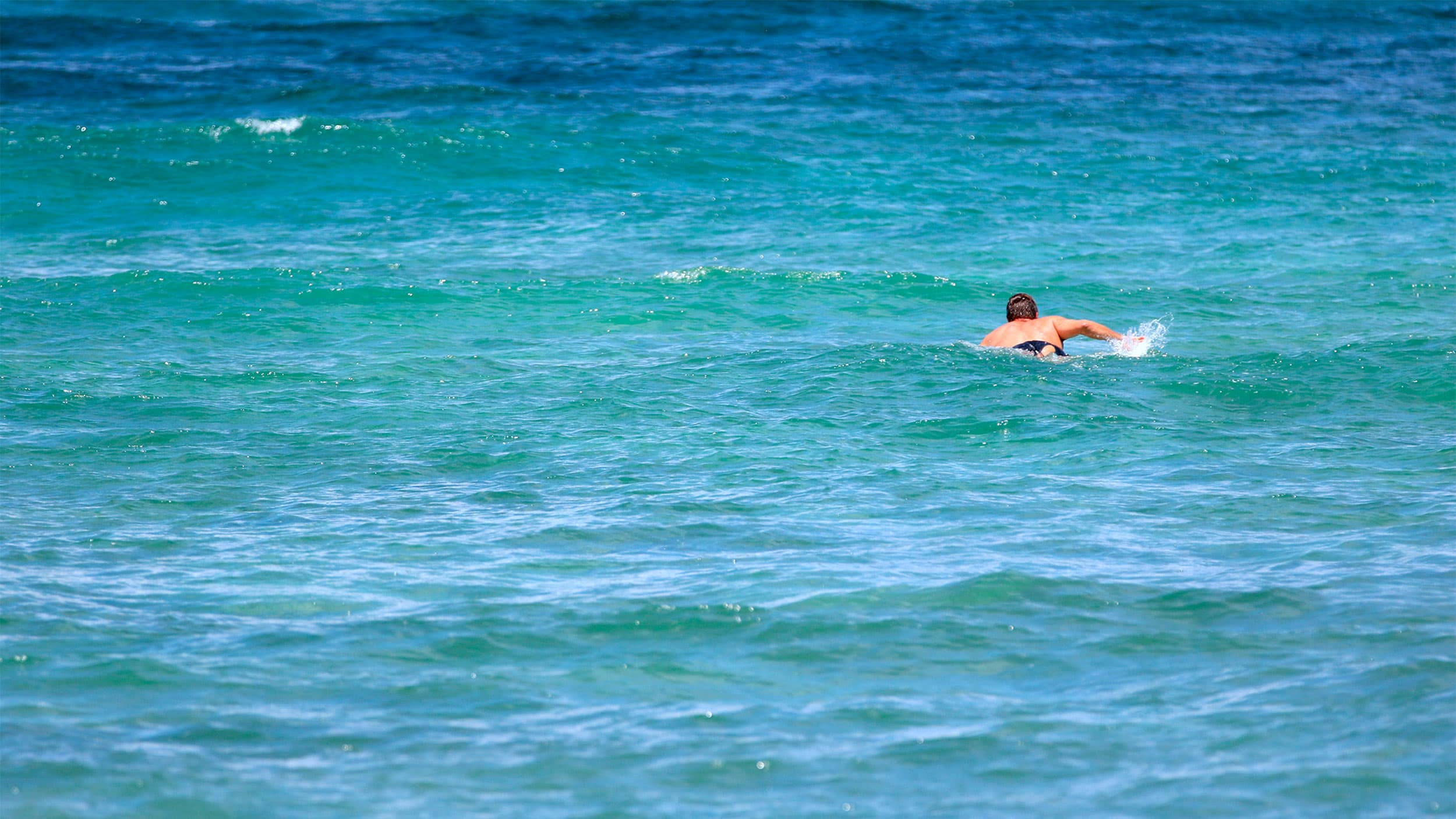 Isaiah Helekunihi Walker paddles out to the blue and green surf in Laie, Hawaii