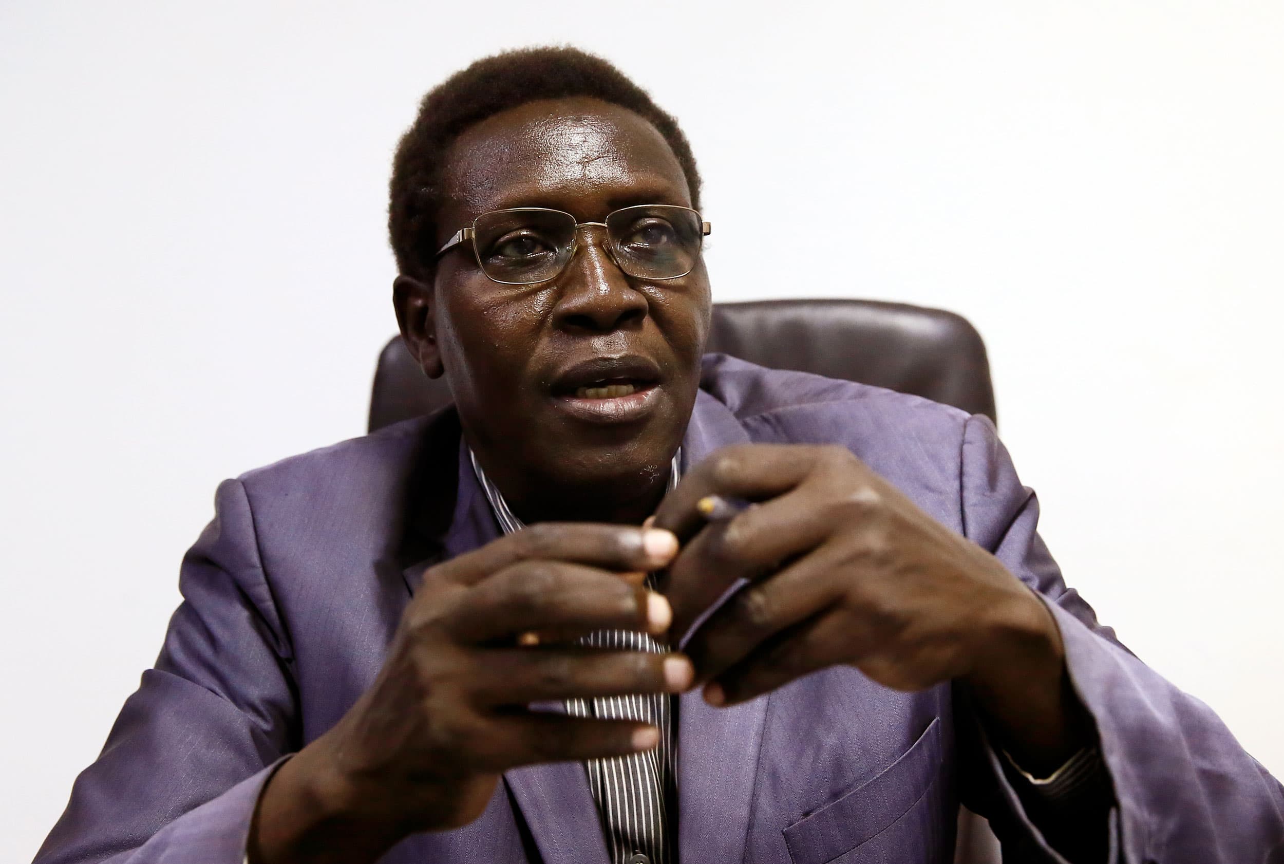 A man is shown wearing a purple suit jacket and wearing glasses.