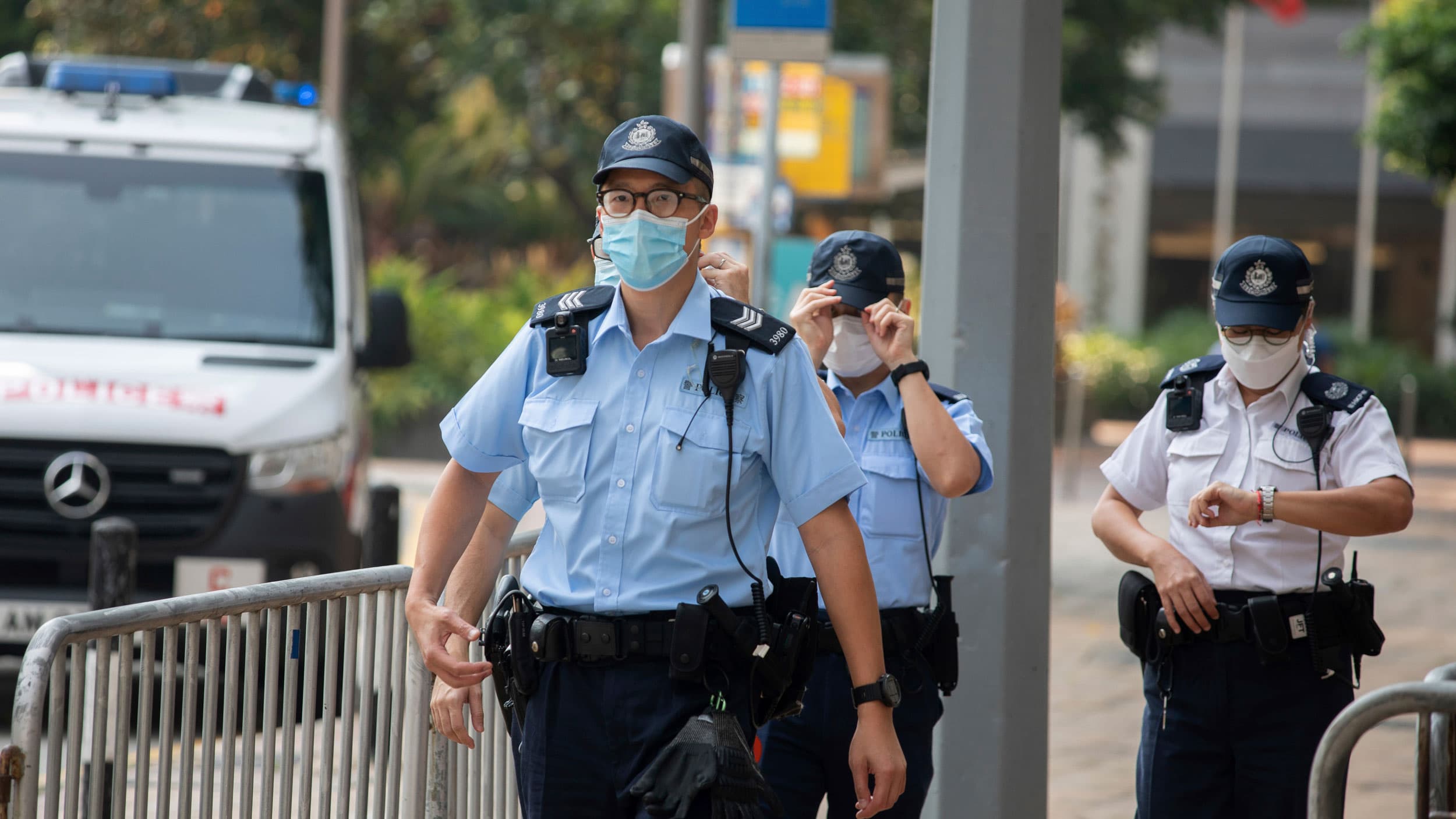 Three police officers are shown, two wearing blue uniforms and the third wearing a white uniform.