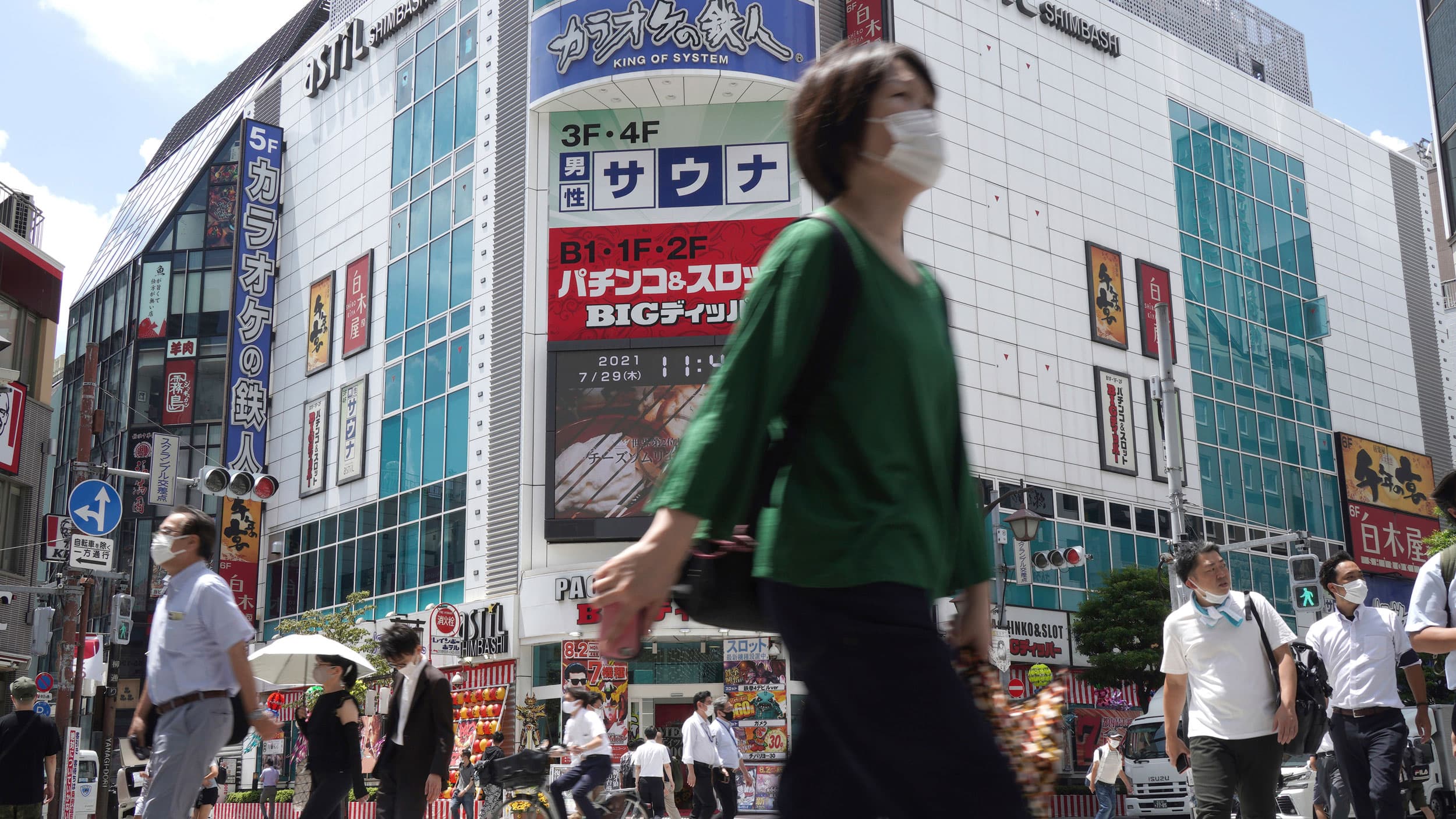 A crowd of people are show walking in various directions outside of a railway station in Tokyo with tall buildings in the background.