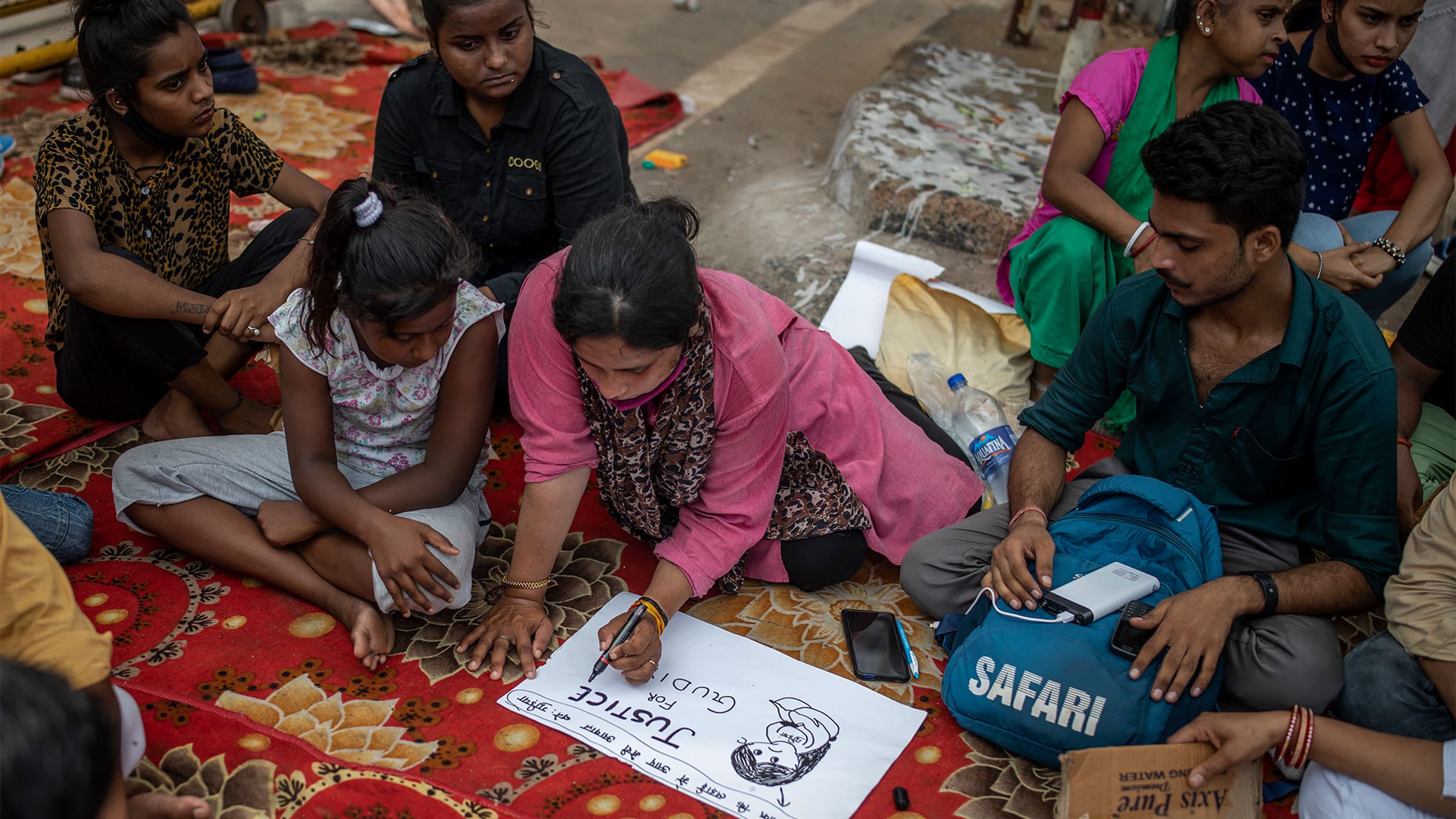 A woman surrounded by other people writes on a white placard