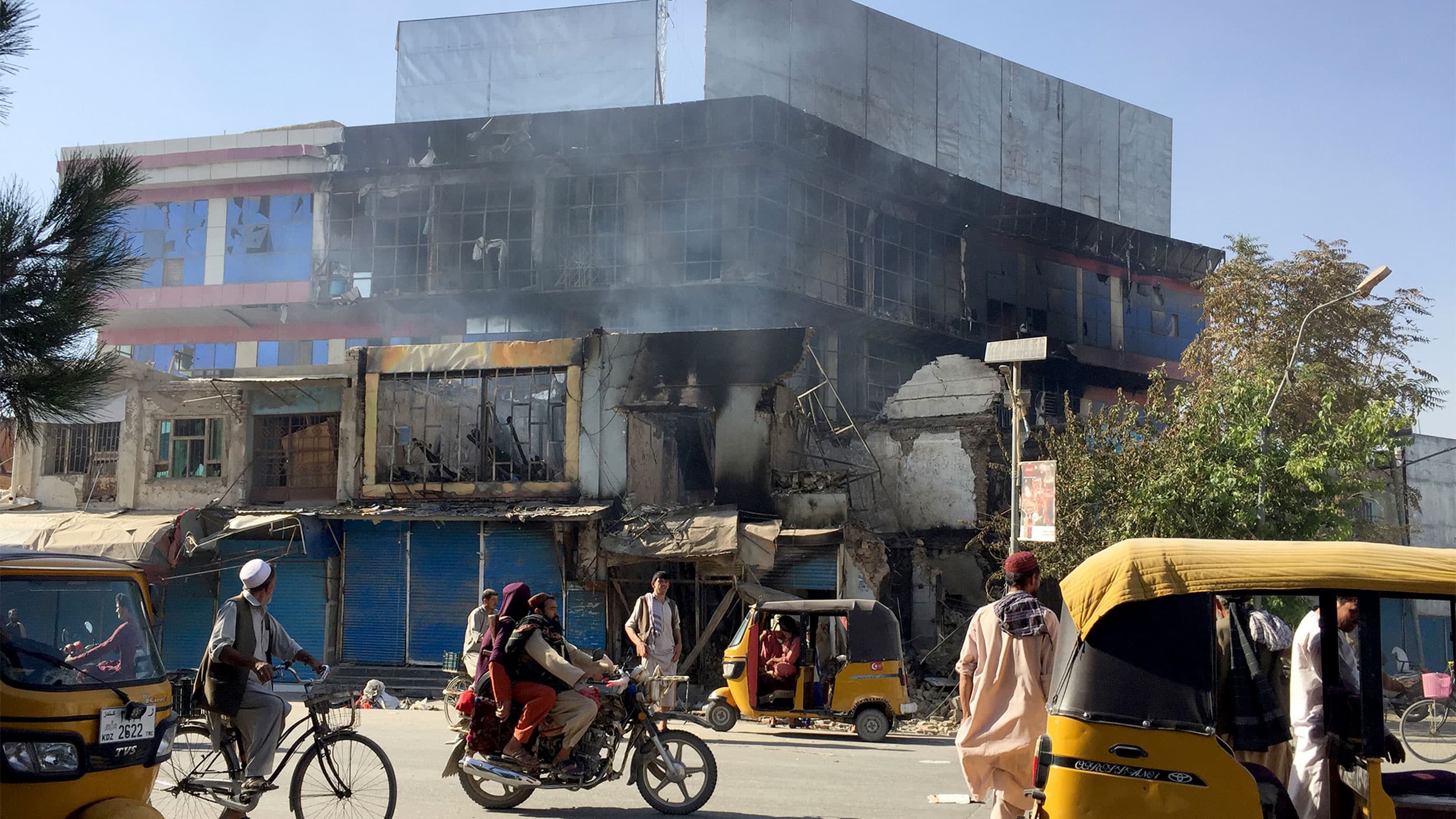 Yellow transport vehicles and people on bikes or standing in front of a smoking building