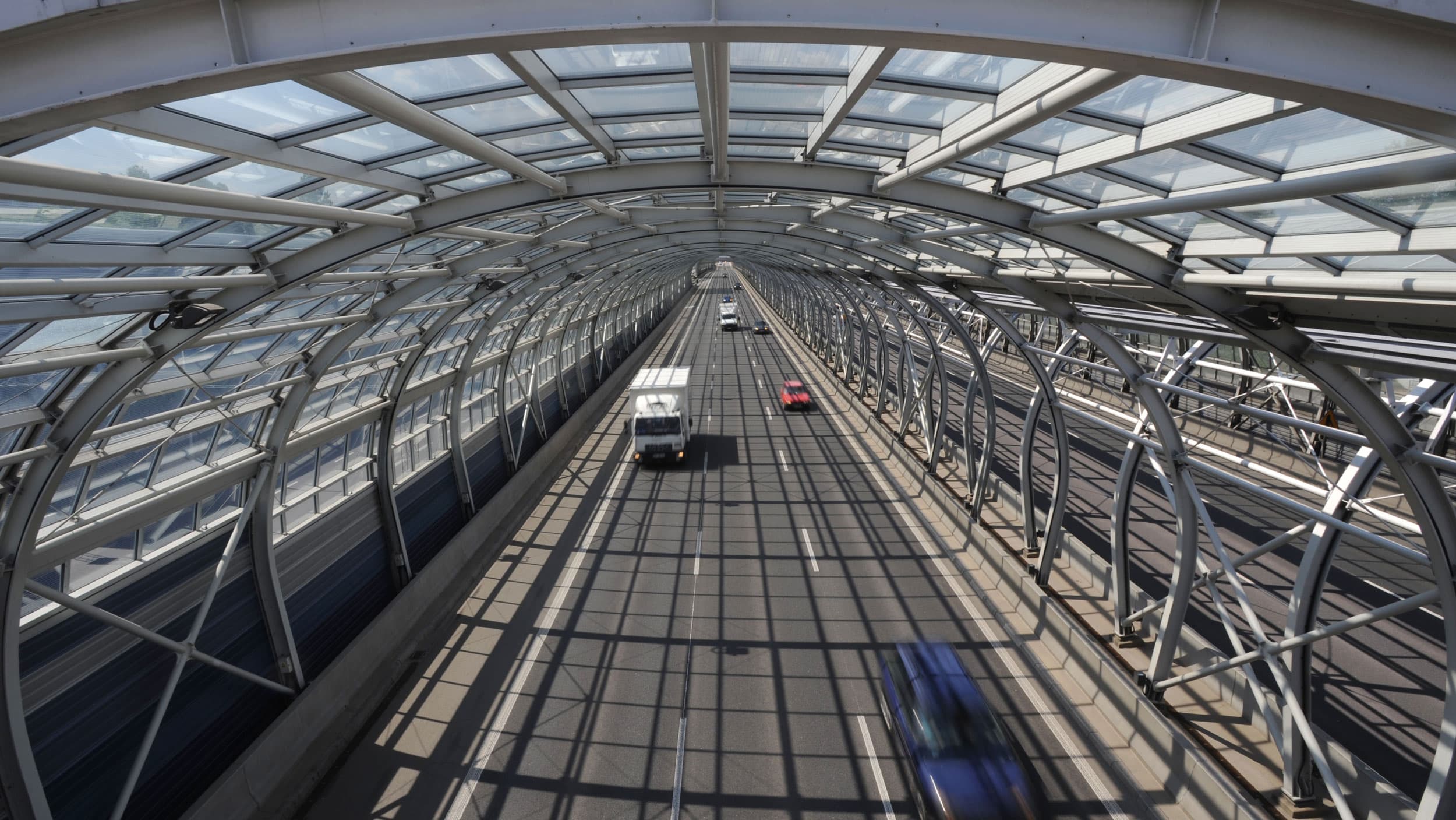 Several vehicles are shown in blurred motion driving on a highway with a circular metal arch over the top.