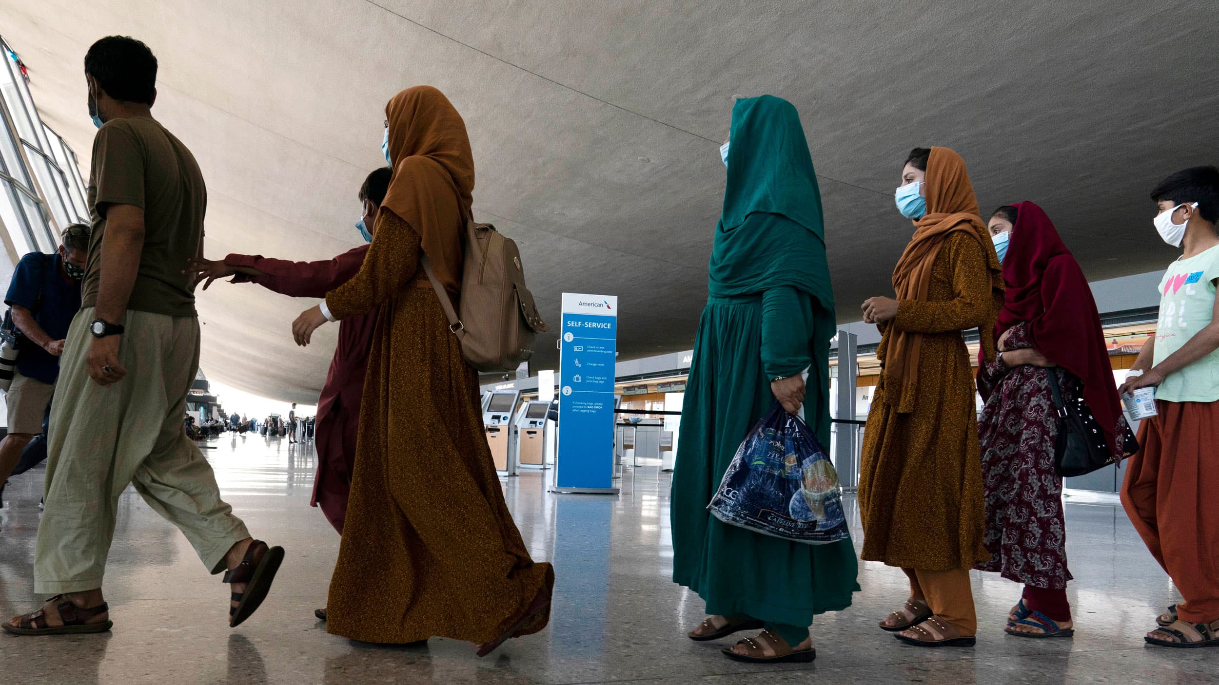 Families evacuated from Kabul, Afghanistan, walk through the terminal before boarding a bus after they arrived at Washington Dulles International Airport, in Chantilly, Virginia, on Friday, Aug. 27, 2021. 