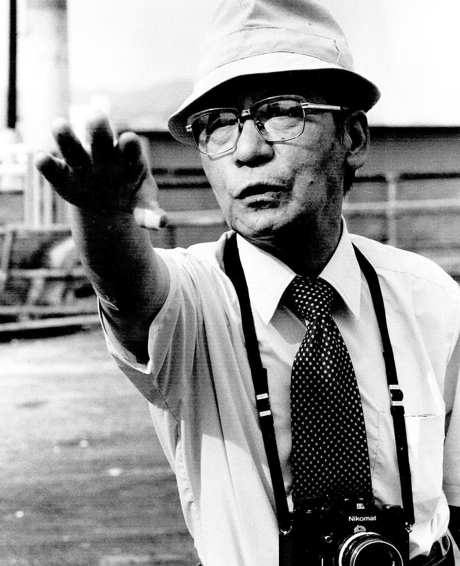 Yoshito Matsushige is shown with this right arm outstretch and a camera hanging from his neck.