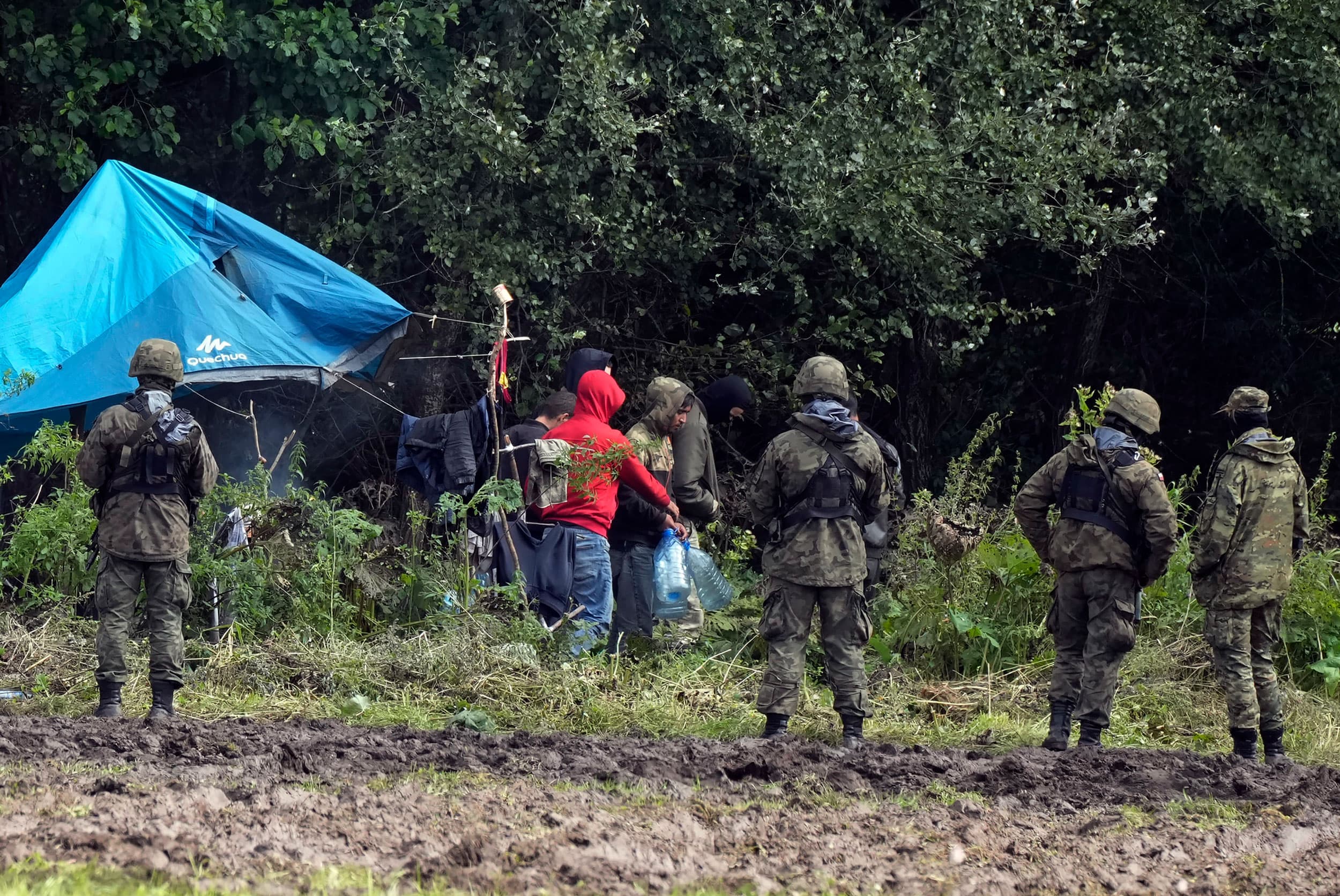 Migrants stuck along the Poland-Belarus border carry plastic water bottles as they are surrounded by Polish forces in Usnarz Gorny, Poland, on Wednesday, Sept. 1, 2021. 