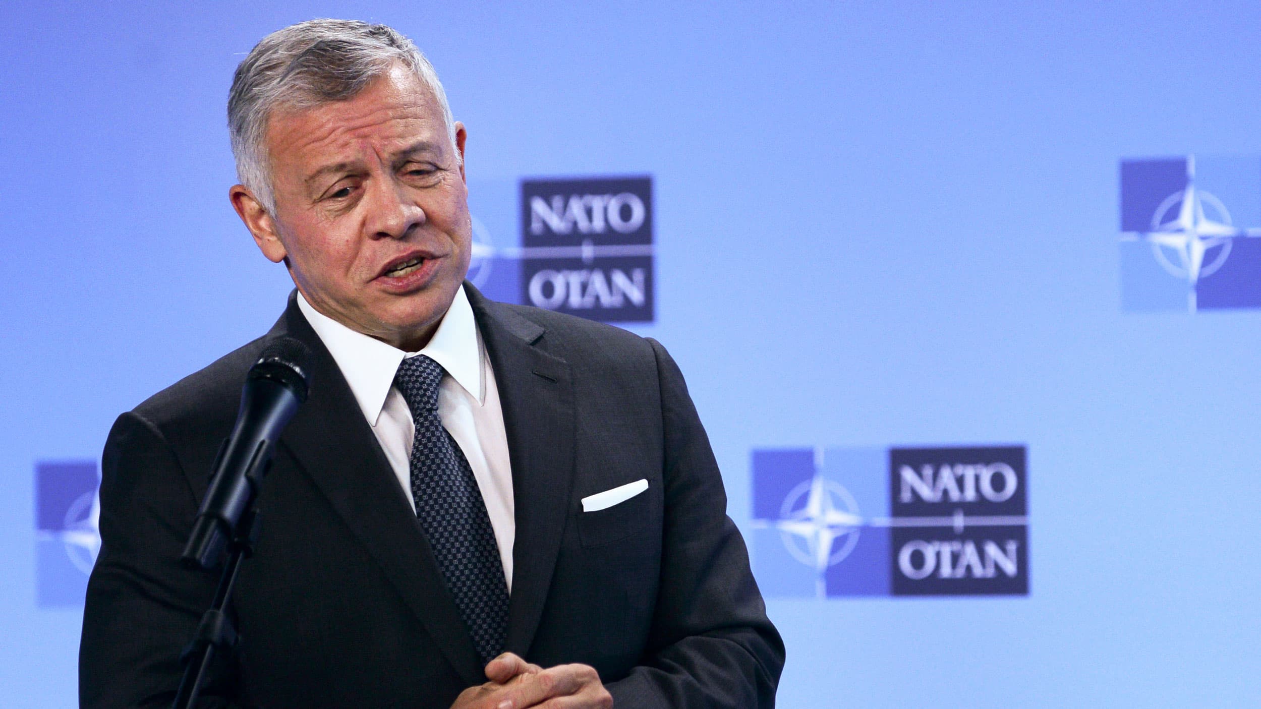 Jordan's King Abdullah II is shown speaking behind a microphone and wearing a dark suit.