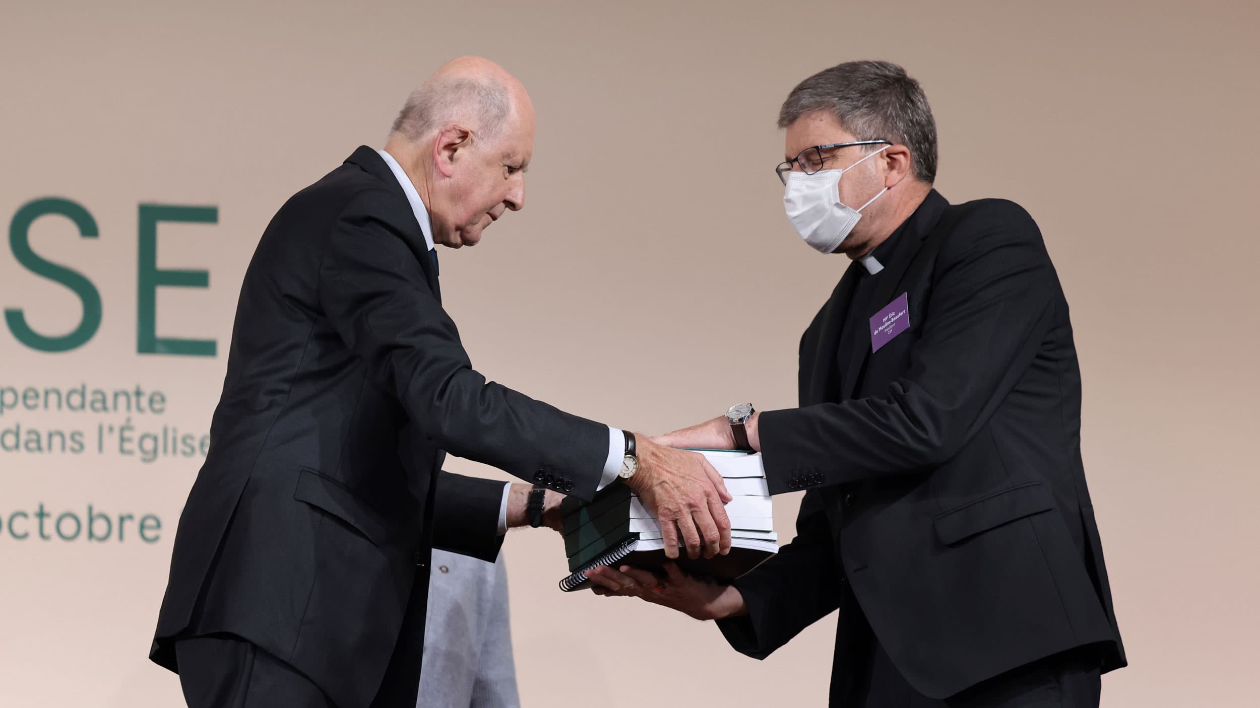 Two men are shown standing across from each other with one man handing a large stack of documents over to the other.
